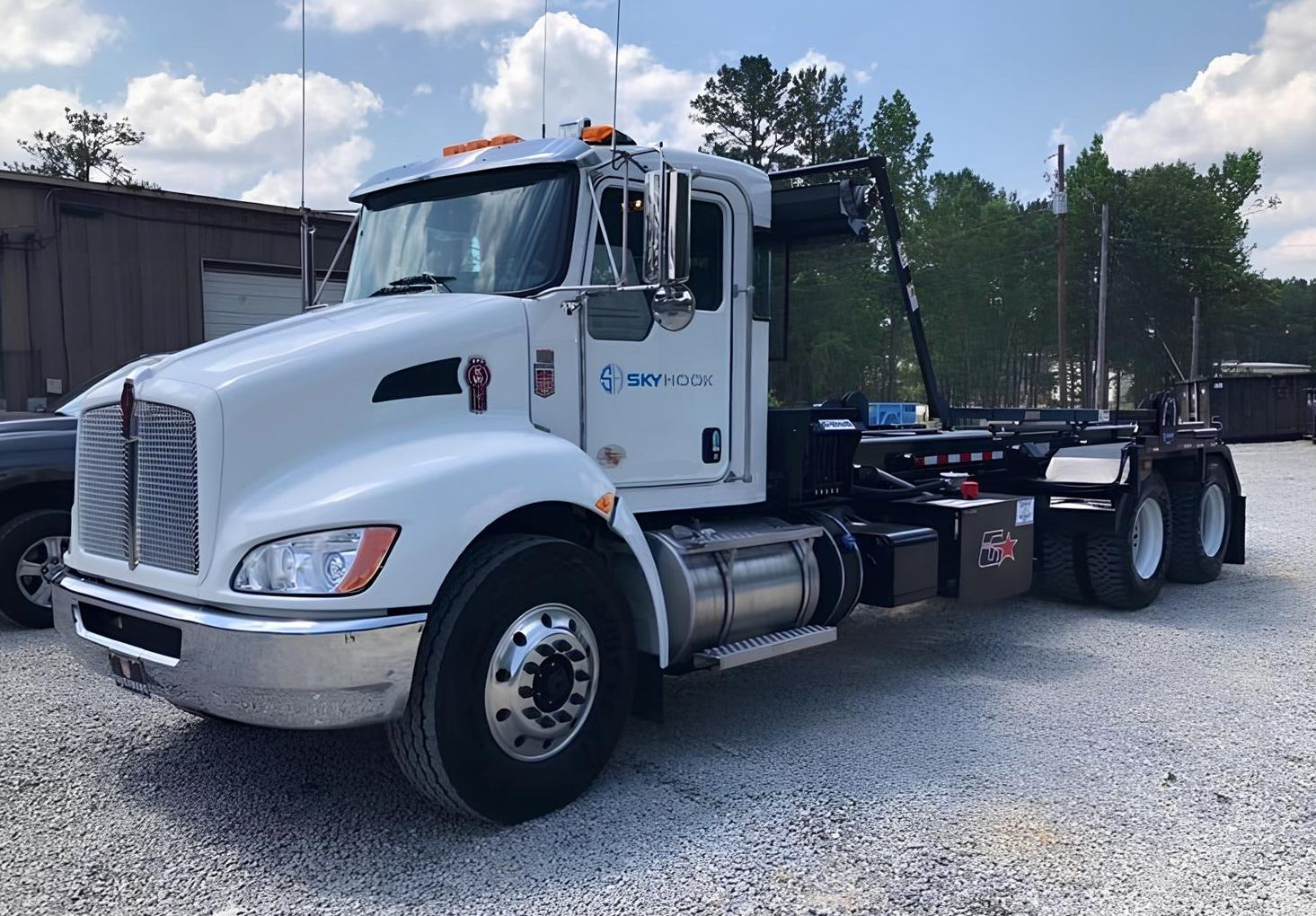 White Kenworth roll-off truck parked on gravel, blue sky in the background.