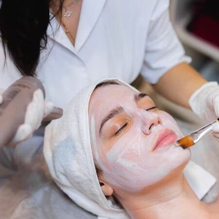 Woman receiving facial treatment in a spa. Cream is being applied to her face with a brush.