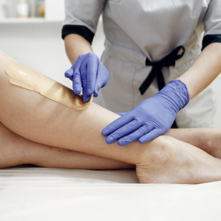 A person's leg being waxed by a gloved technician. A strip of wax is being applied to the skin.