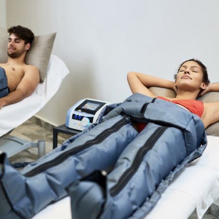 Two people relaxing with compression therapy on their legs; indoors, white walls.