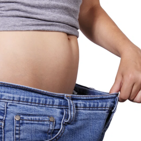 Person with a bare midriff wearing oversized jeans, showing weight loss.