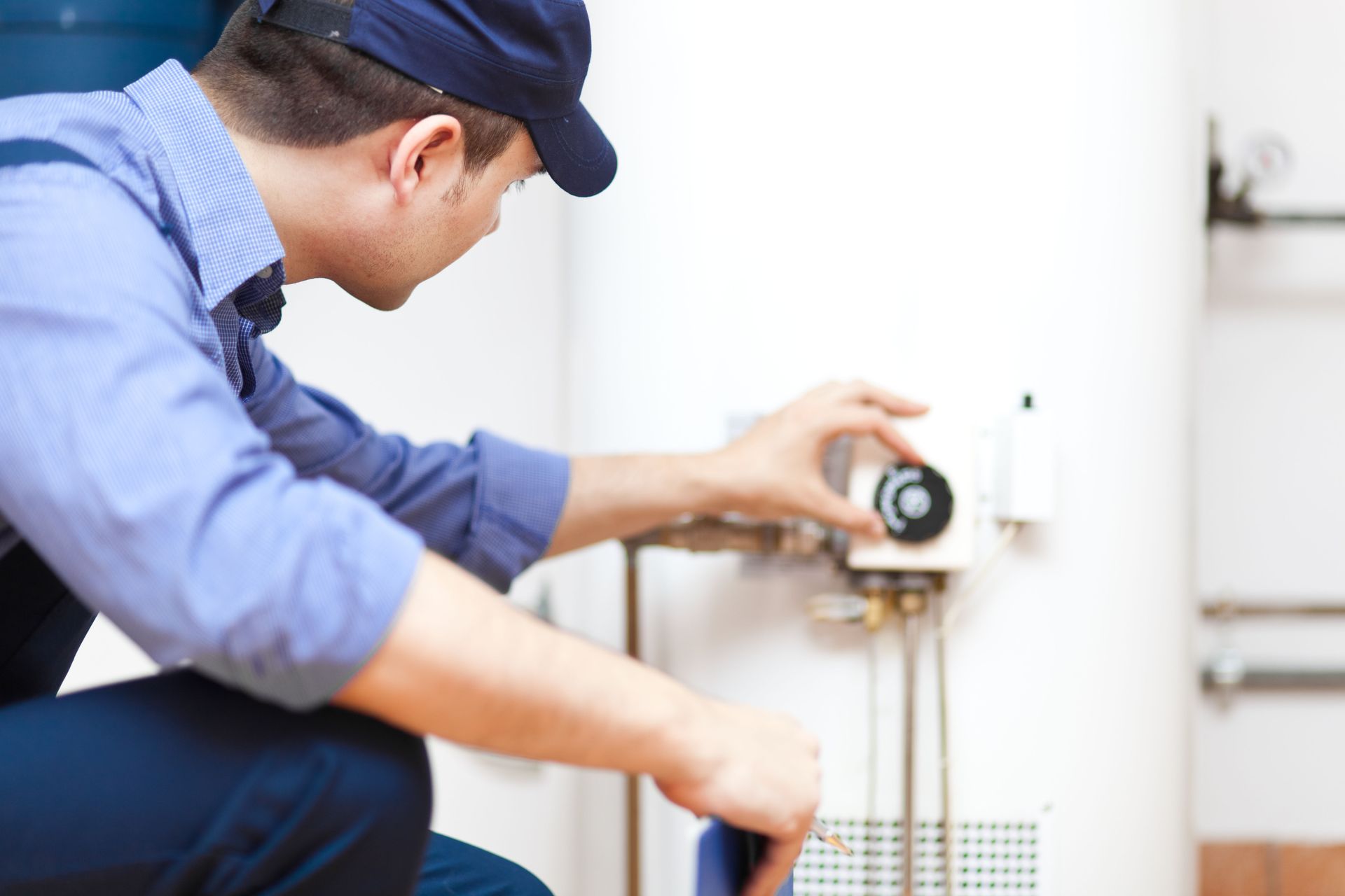 Plumber adjusting a water heater thermostat in a white utility room.