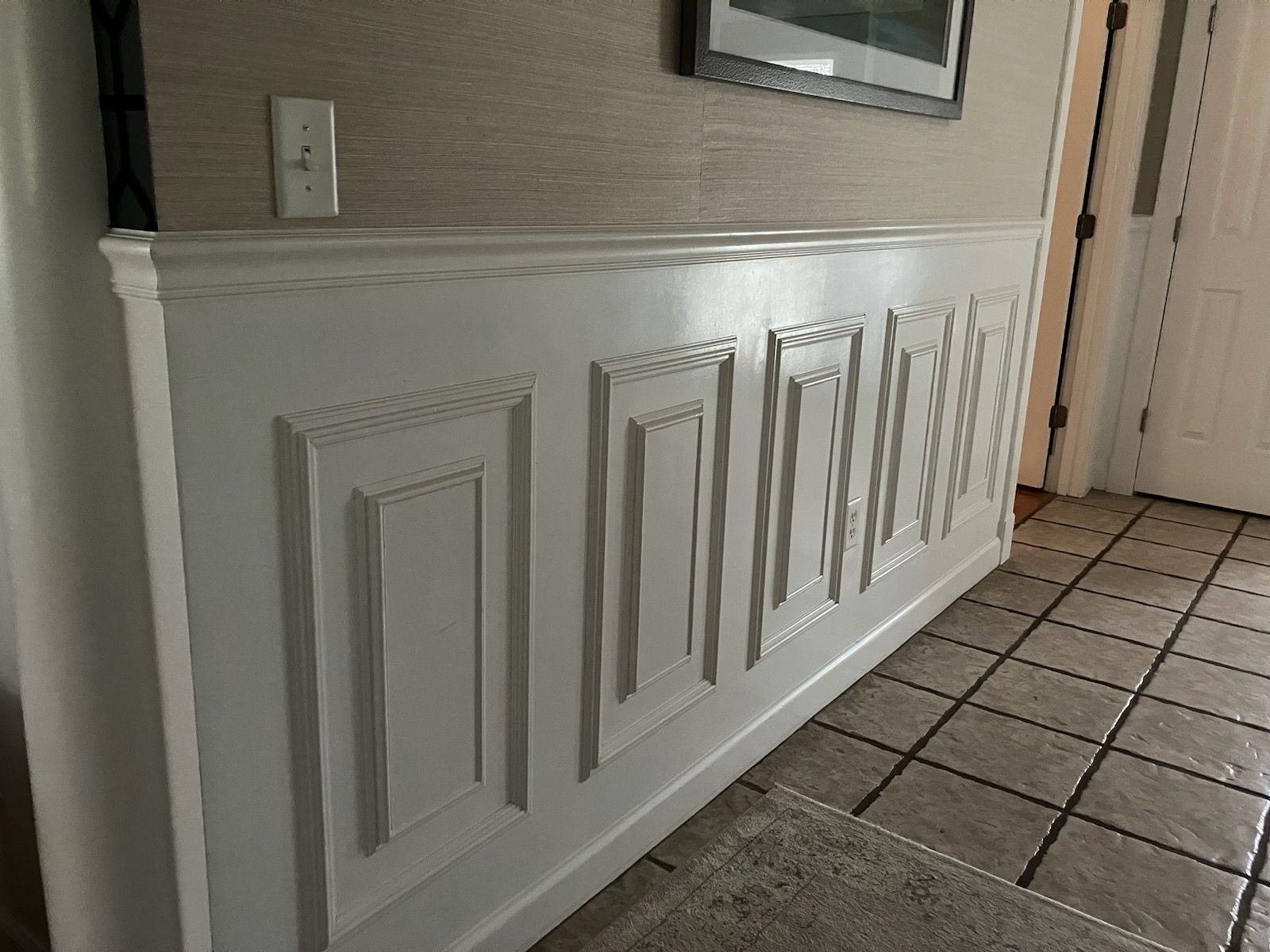 A hallway with a picture on the wall and a tile floor.