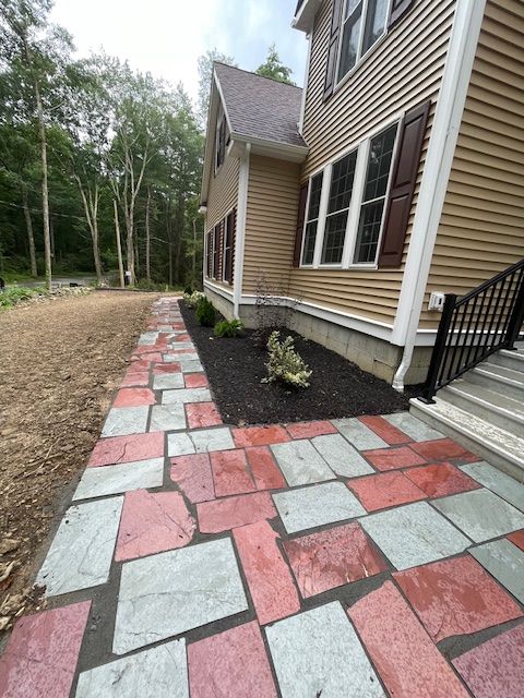 A brick walkway leading to a house with trees in the background.