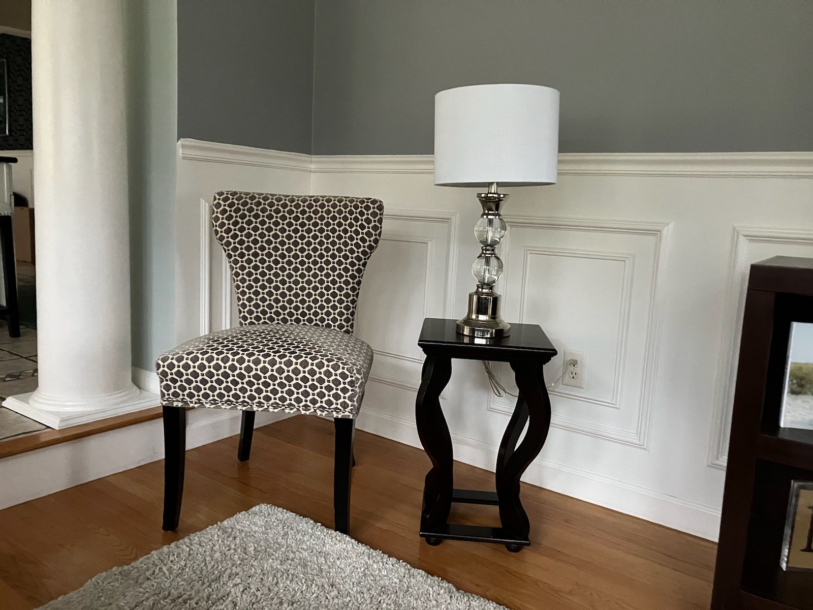 A chair is sitting next to a lamp on a table in a living room.