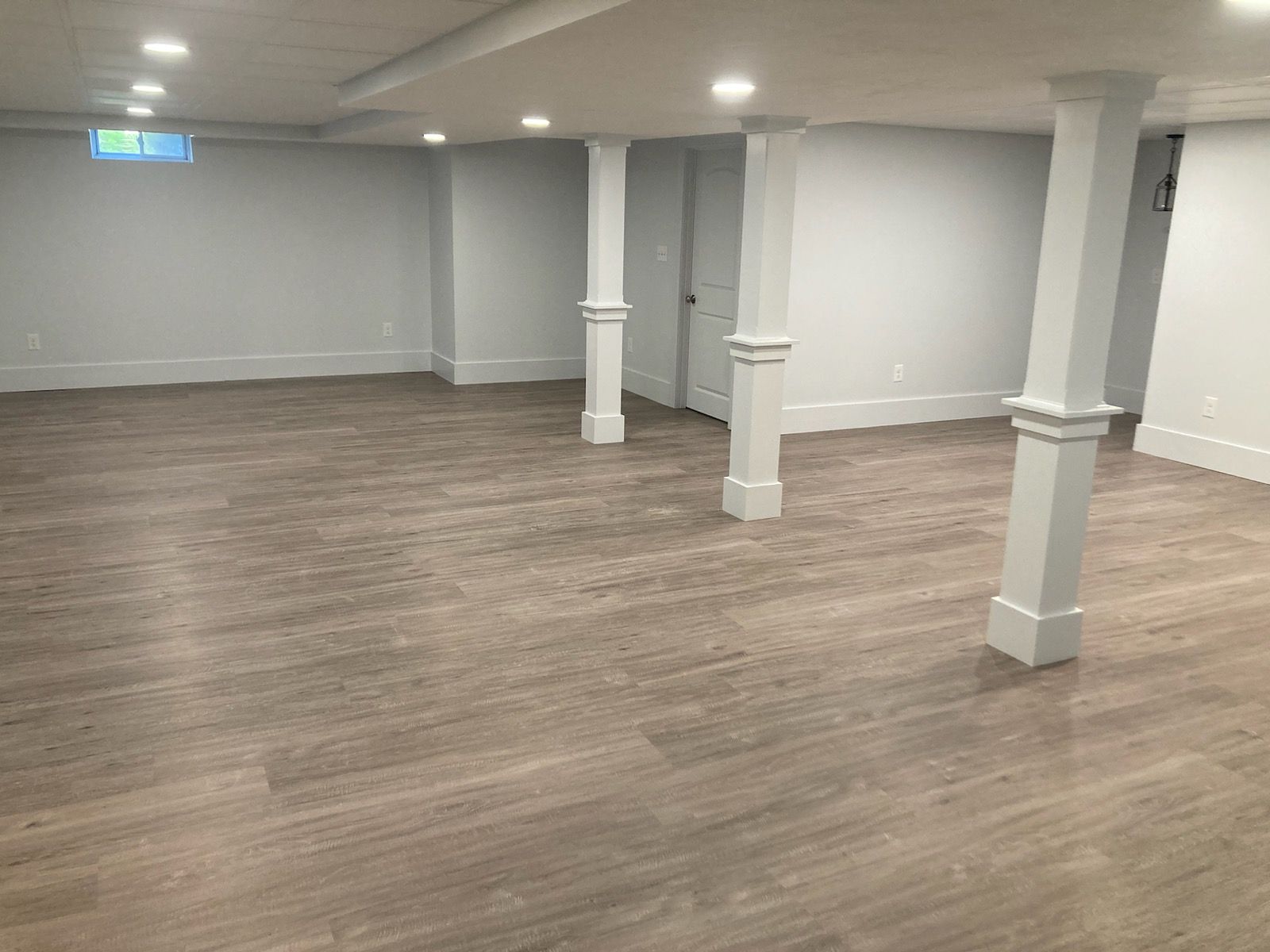 An empty basement with hardwood floors and white pillars.