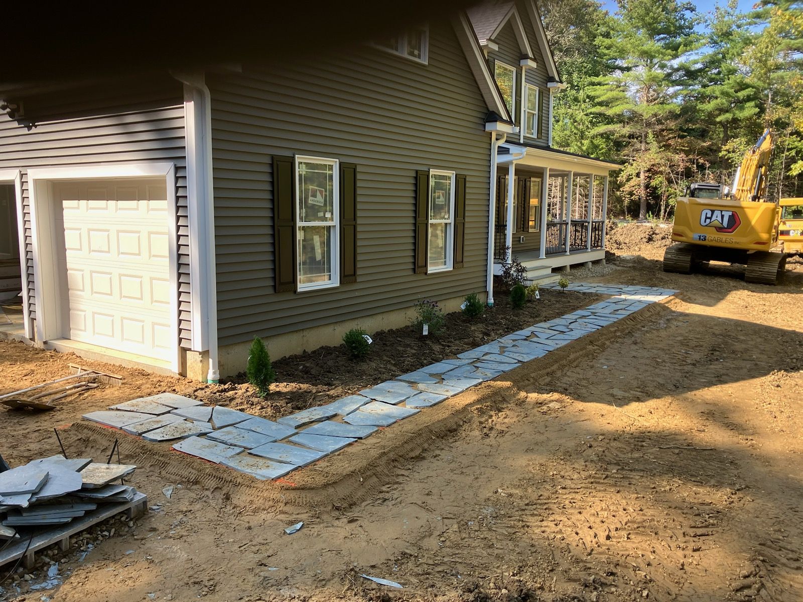 A cat excavator is parked in front of a house under construction.