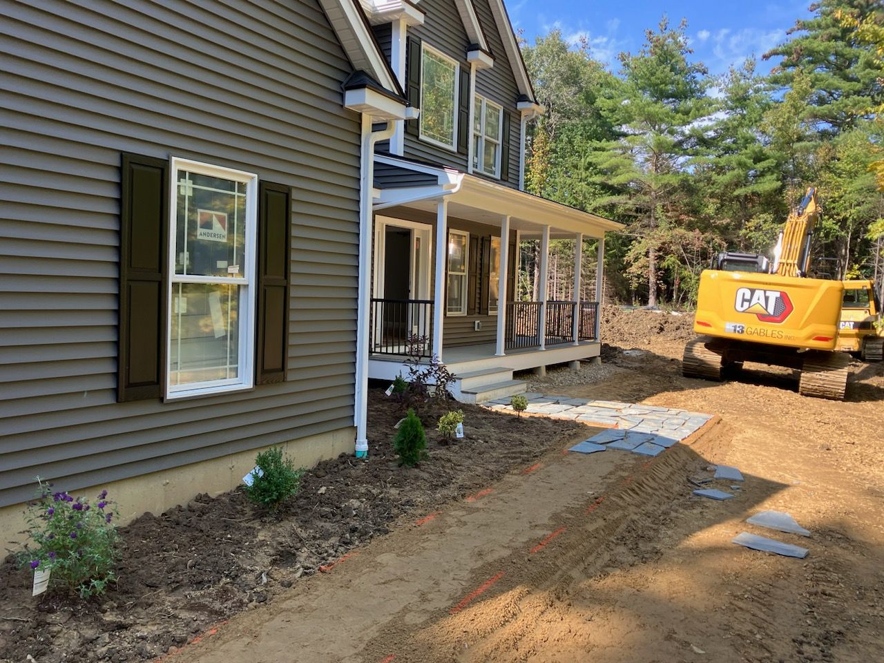 A house with a cat excavator in front of it.