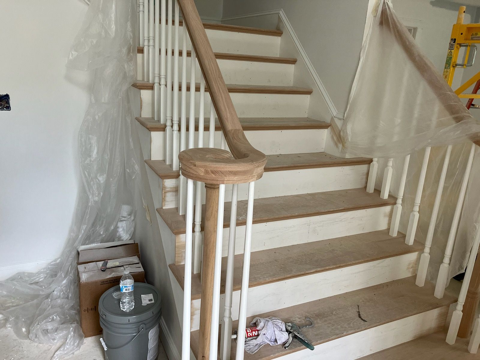 A staircase is being painted in a room with a bucket and a bottle of water.