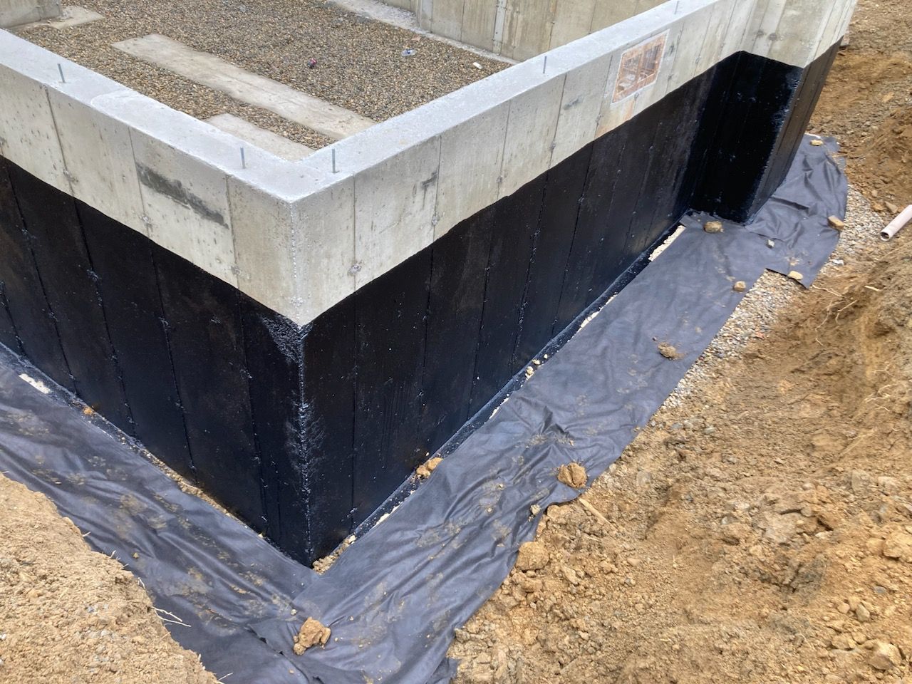 A concrete wall with black waterproofing applied to it.