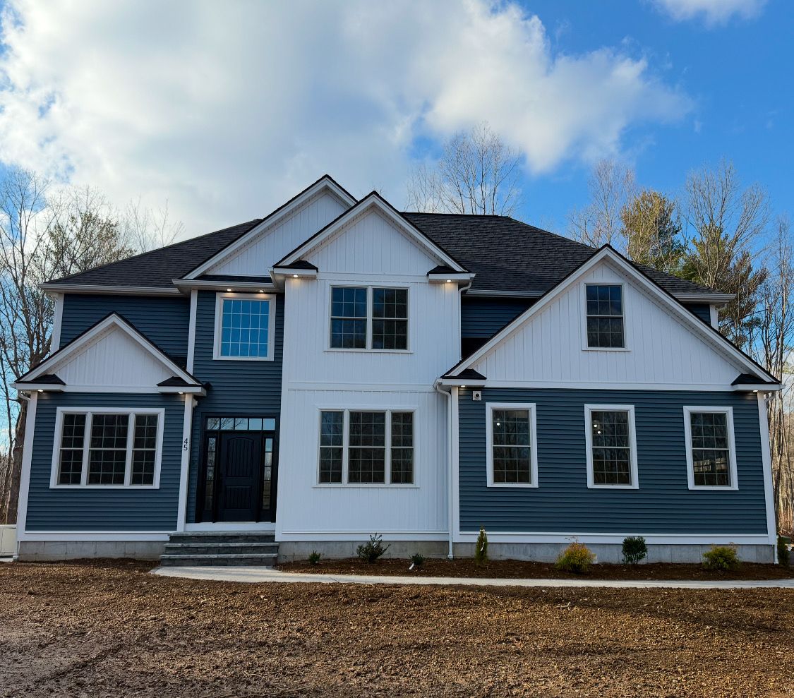 A large house with blue siding and white trim is sitting on top of a dirt field.