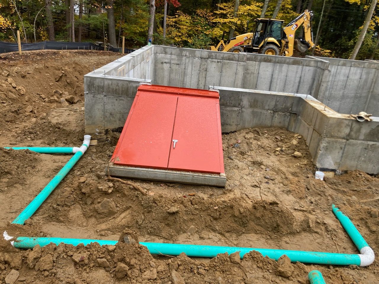 A red door is sitting in the dirt next to a concrete wall.