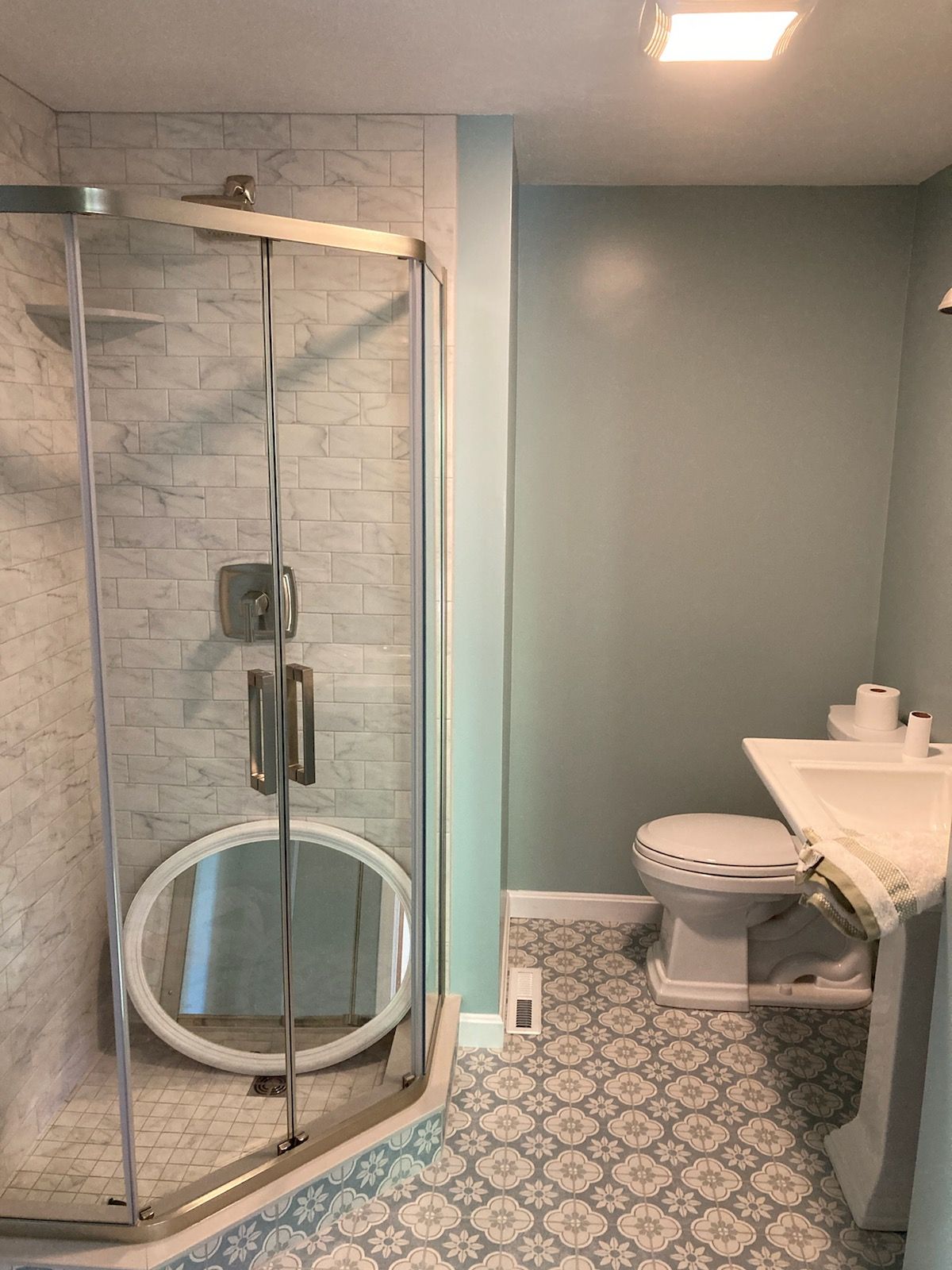A bathroom with a toilet, sink, shower, and mirror.