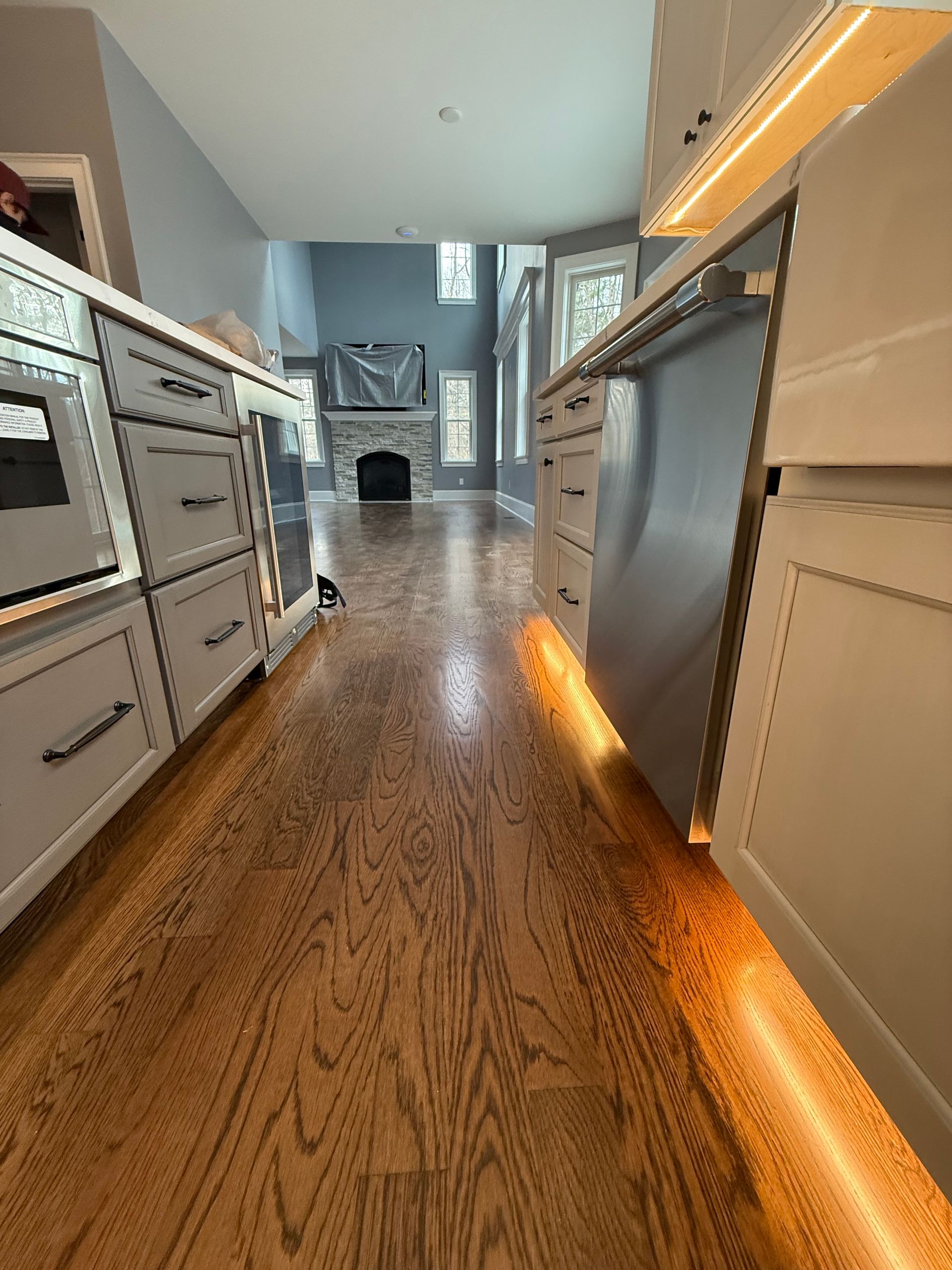 A kitchen with hardwood floors , white cabinets and stainless steel appliances.