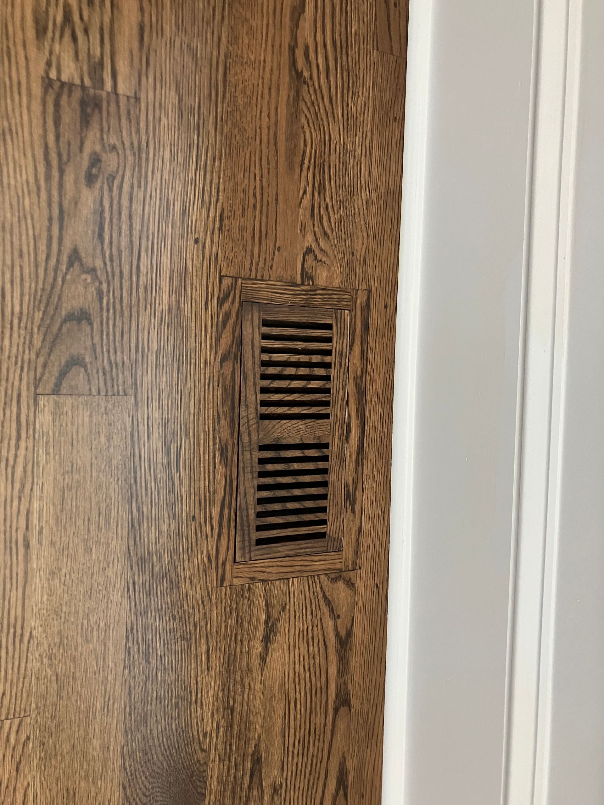 A close up of a wooden floor with a vent on it.