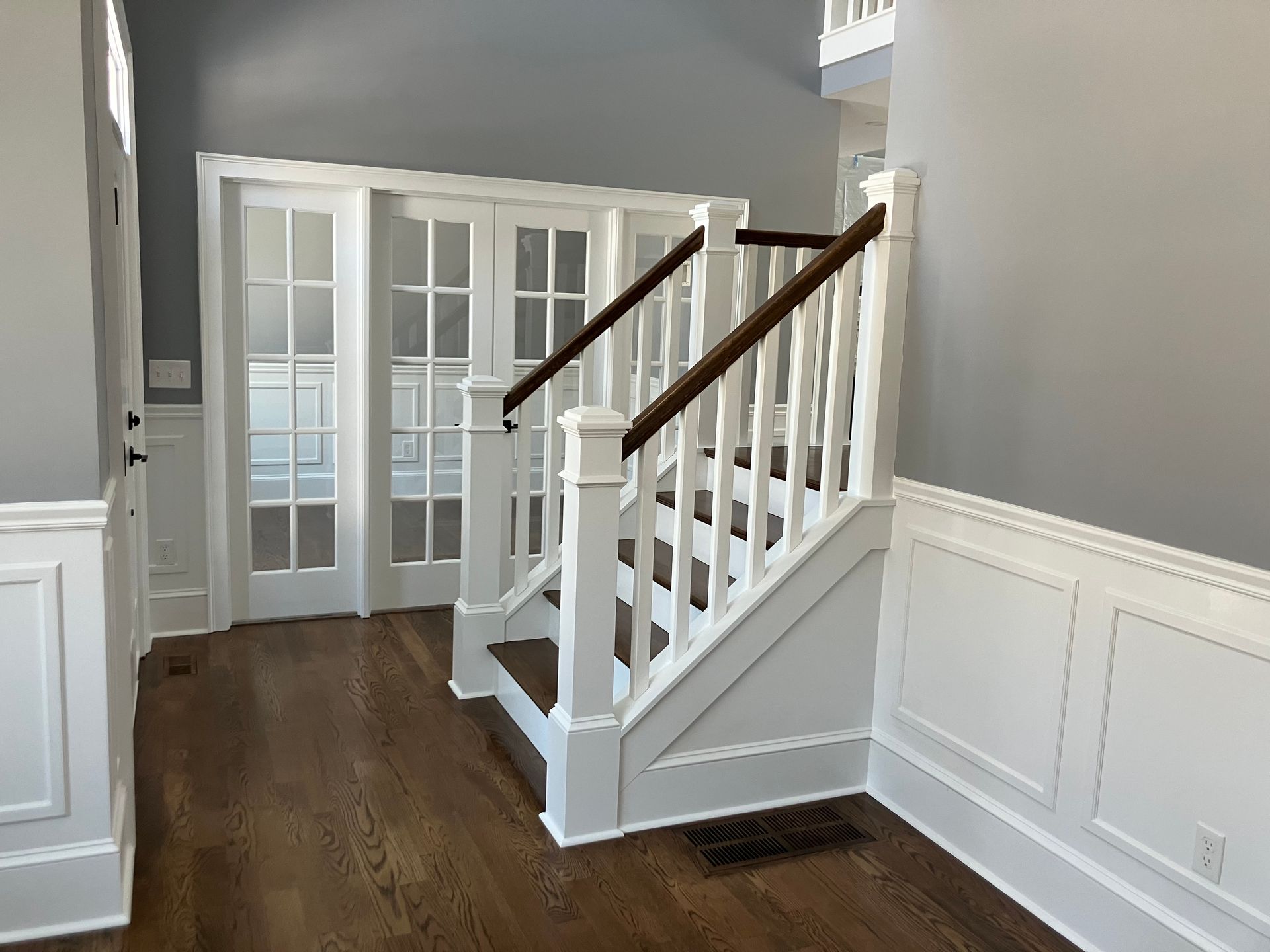 An empty hallway with a staircase and french doors.