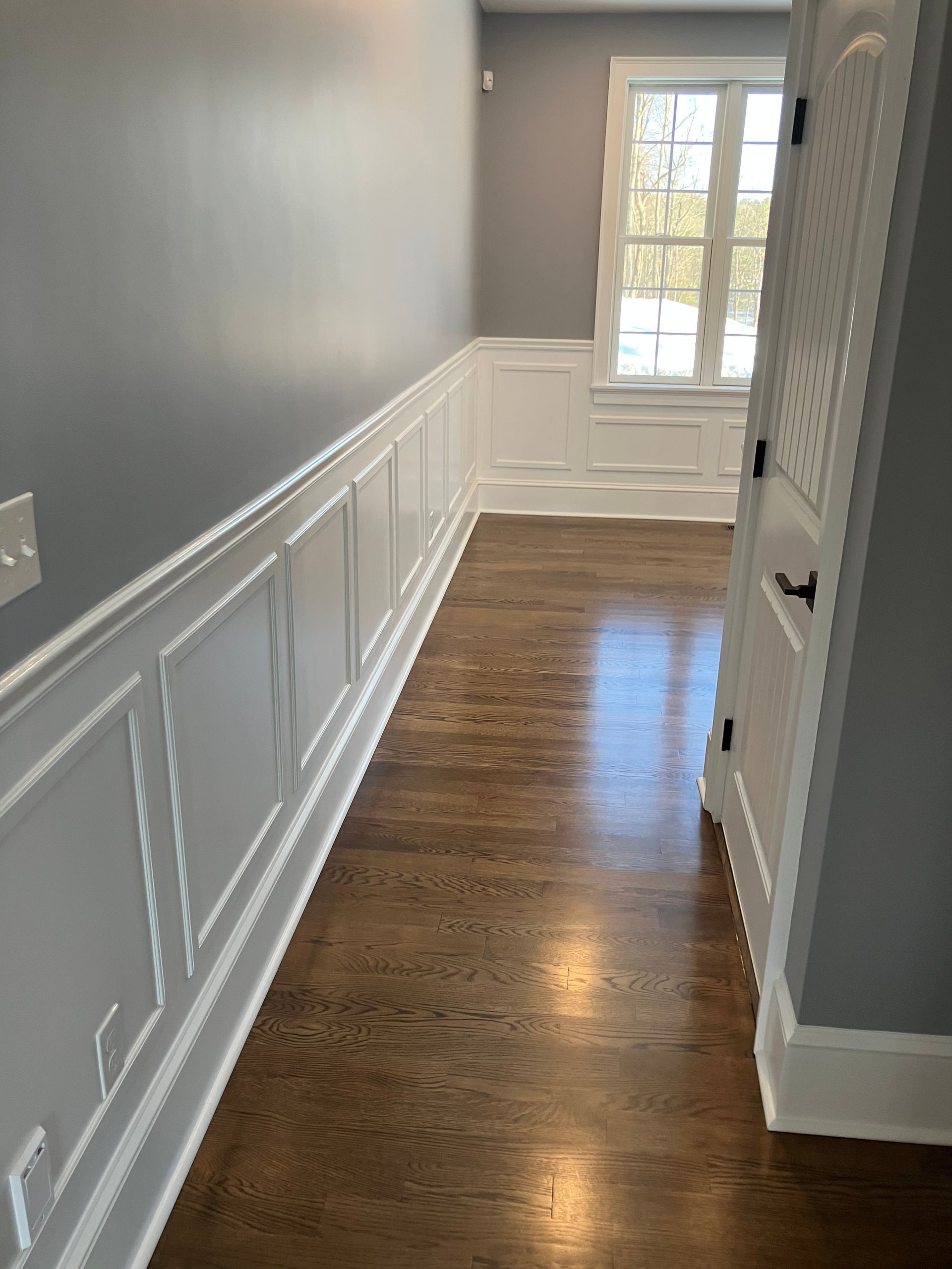 A hallway with hardwood floors and white trim in a house.