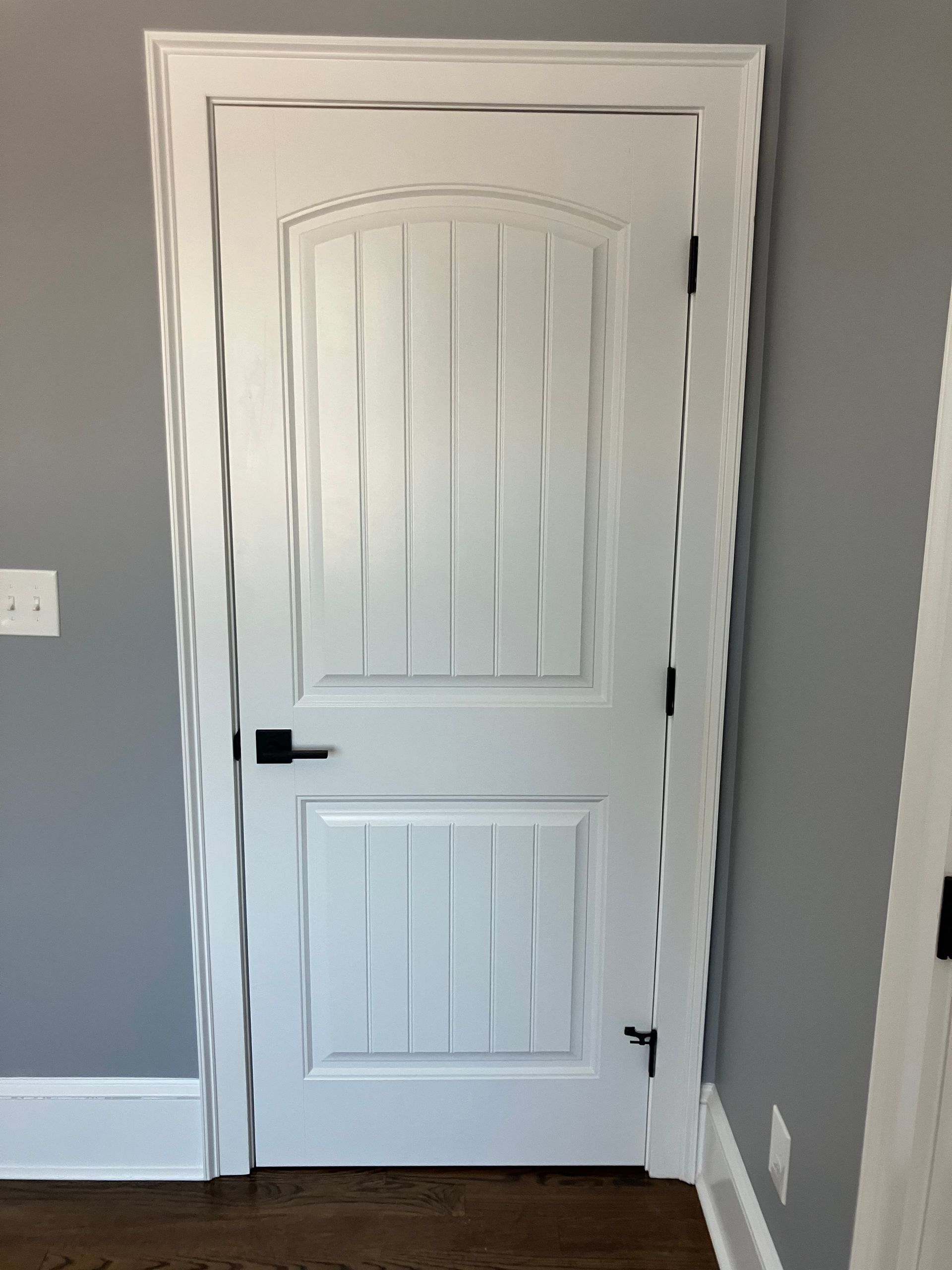A white door with a black handle is in a room with gray walls.