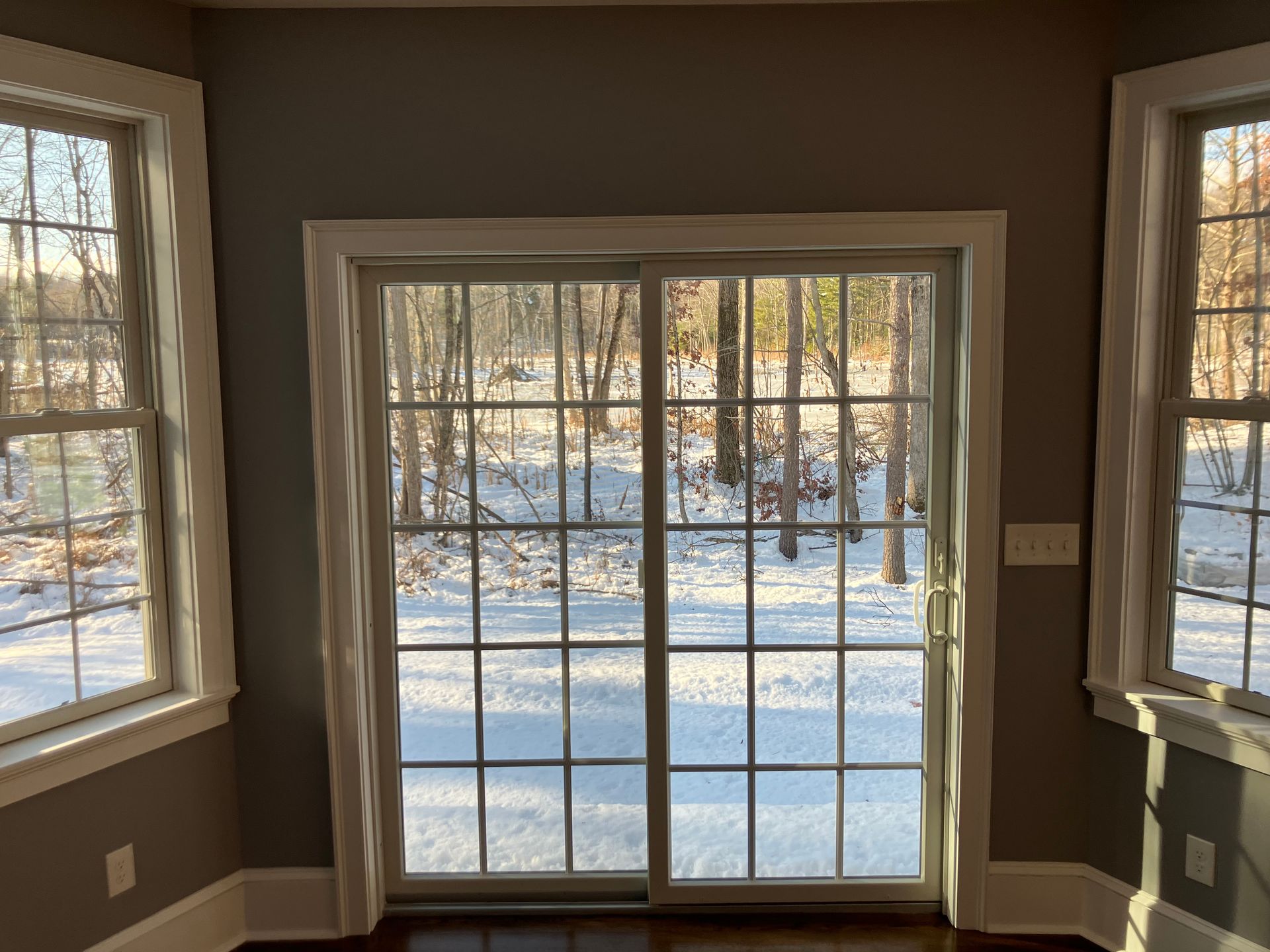 A room with a sliding glass door looking out to a snowy forest.
