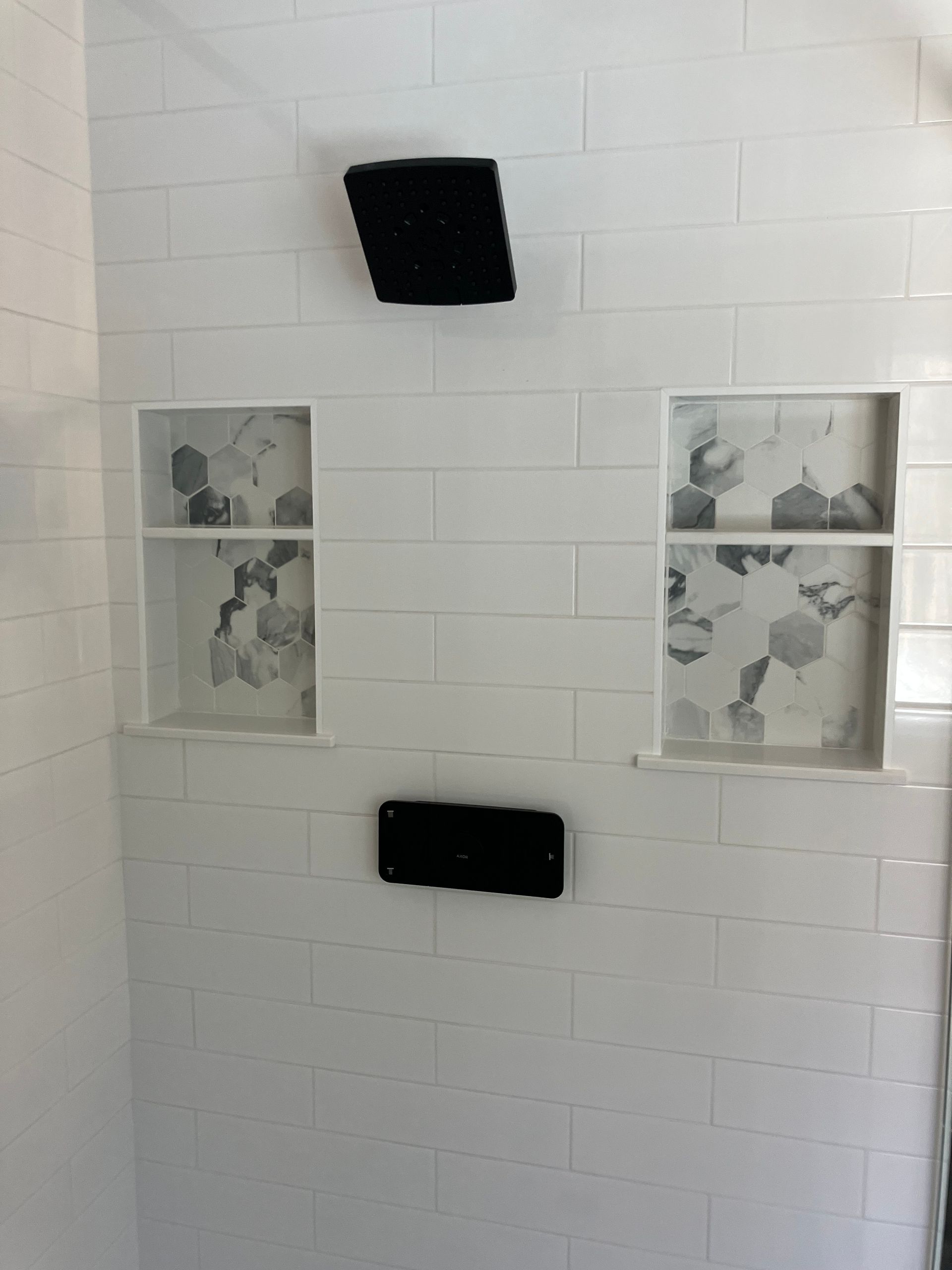 A bathroom with white tiles and a black shower head