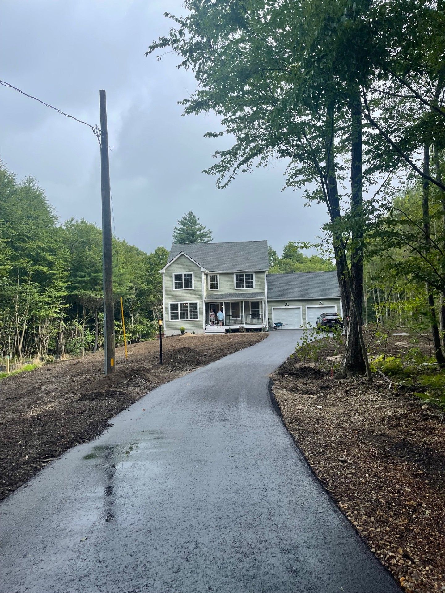 A house with a driveway leading to it is surrounded by trees on a cloudy day.