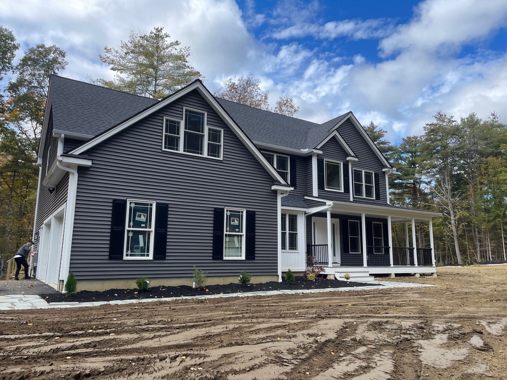 A large house with a large porch is sitting on top of a dirt field.