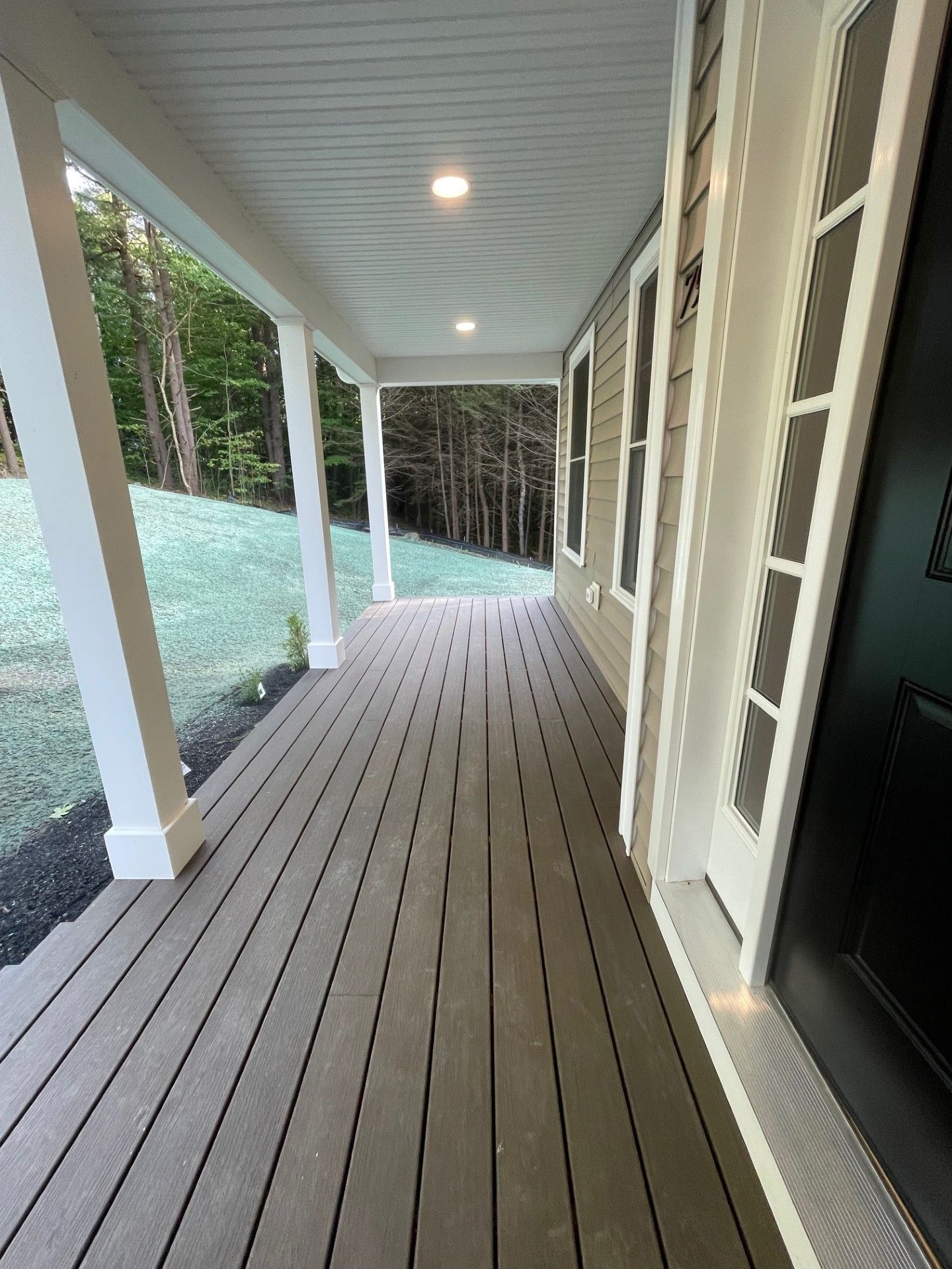 There is a large porch with a lot of windows and trees in the background.