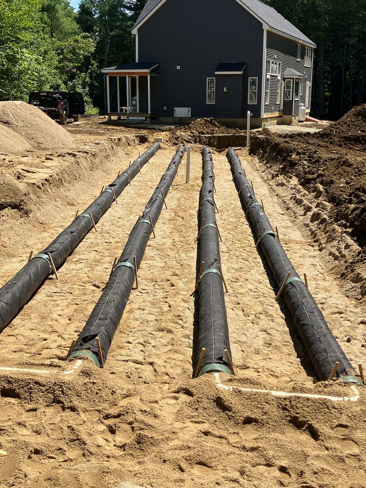 A row of pipes are lined up in the dirt in front of a house.