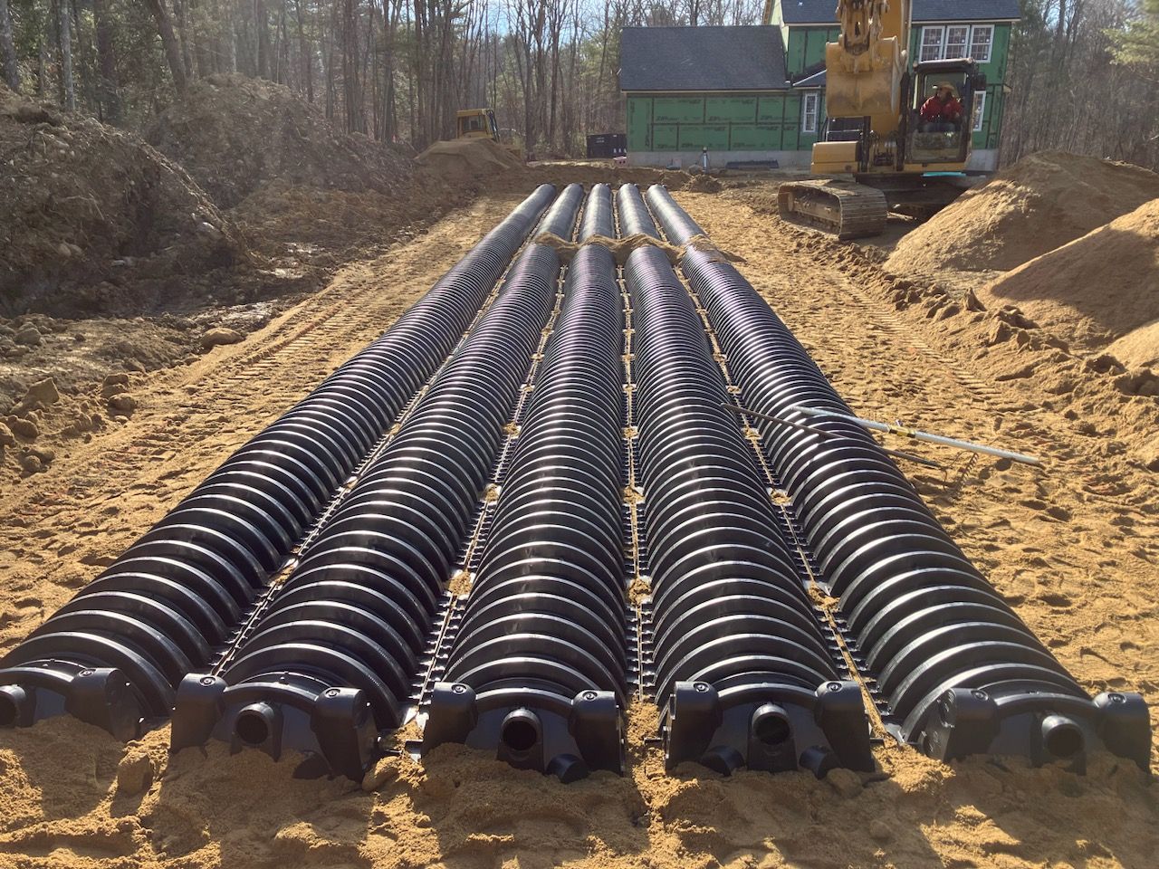 A row of black pipes in the dirt with a bulldozer in the background