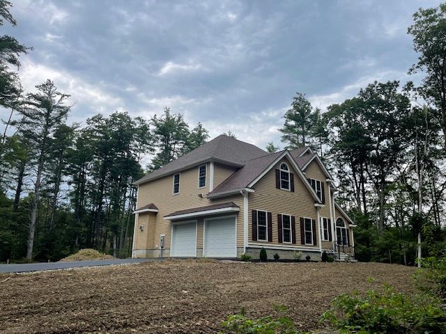 A large house with two garage doors is surrounded by trees.