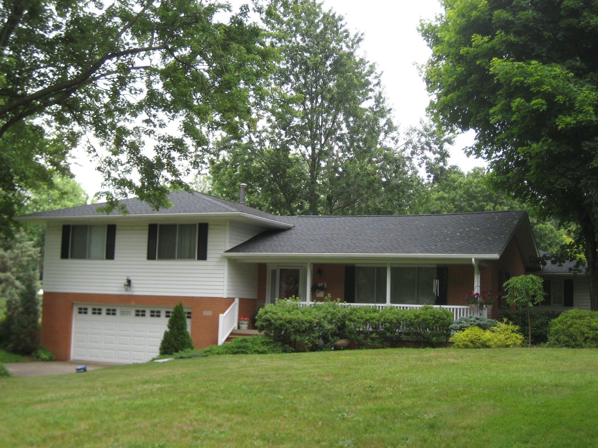 A white house with a black roof is surrounded by trees