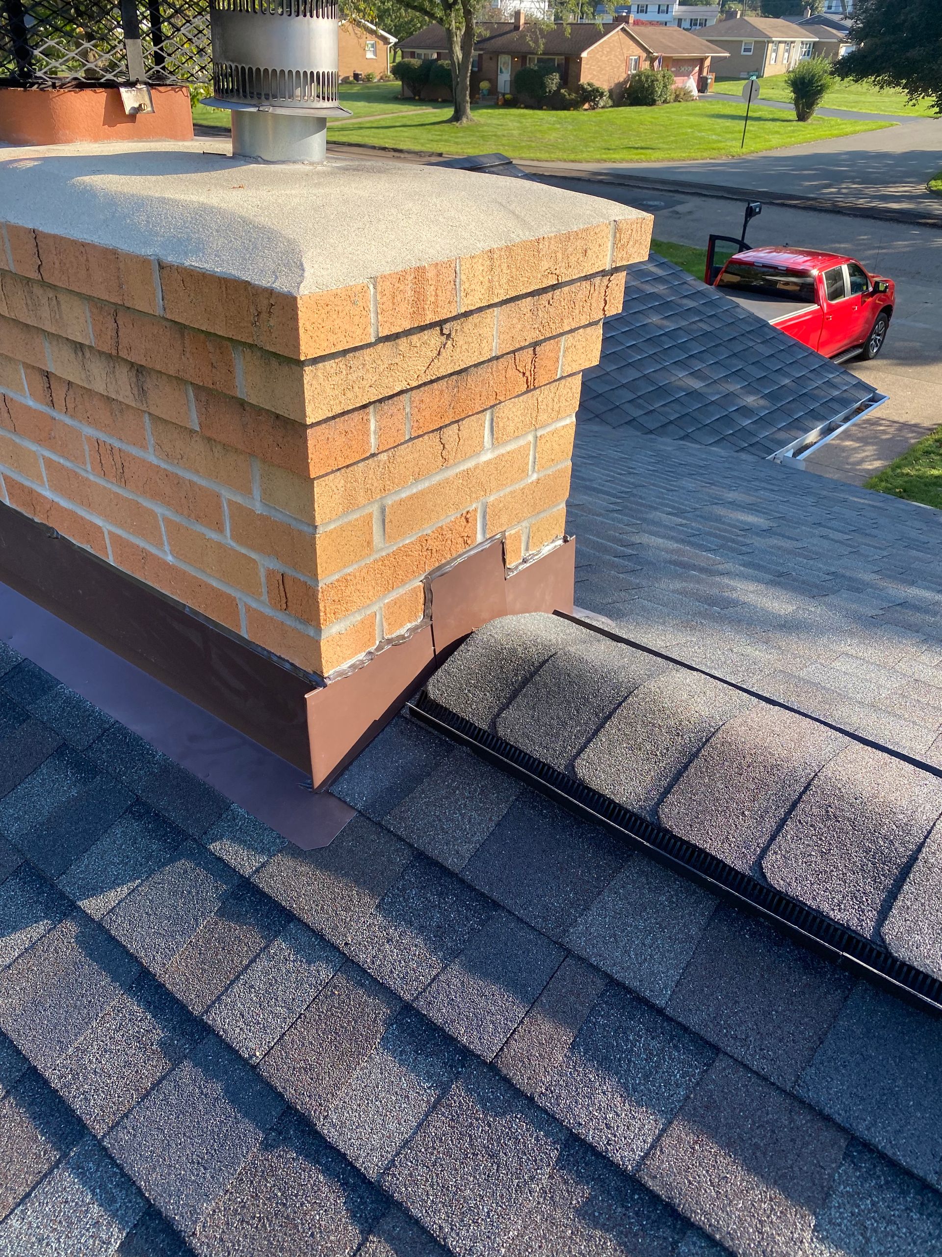 A brick chimney is sitting on top of a roof next to a red truck.