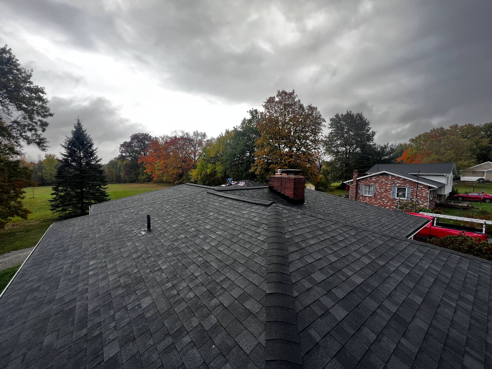 A roof of a house with a chimney and trees in the background on a cloudy day.