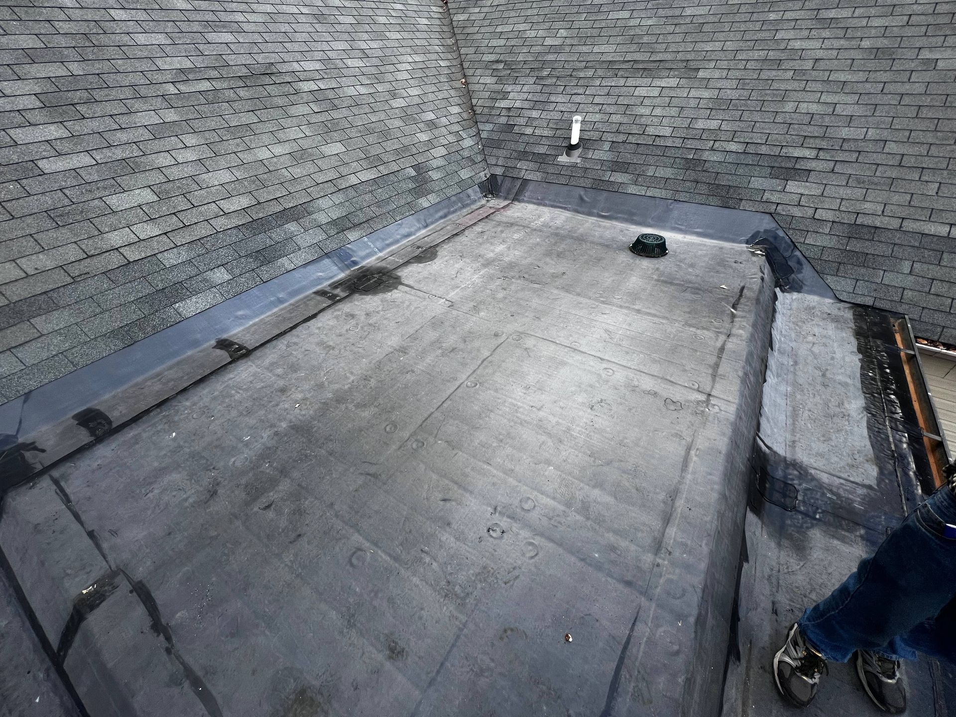 A person is standing on a roof with a brick wall in the background.