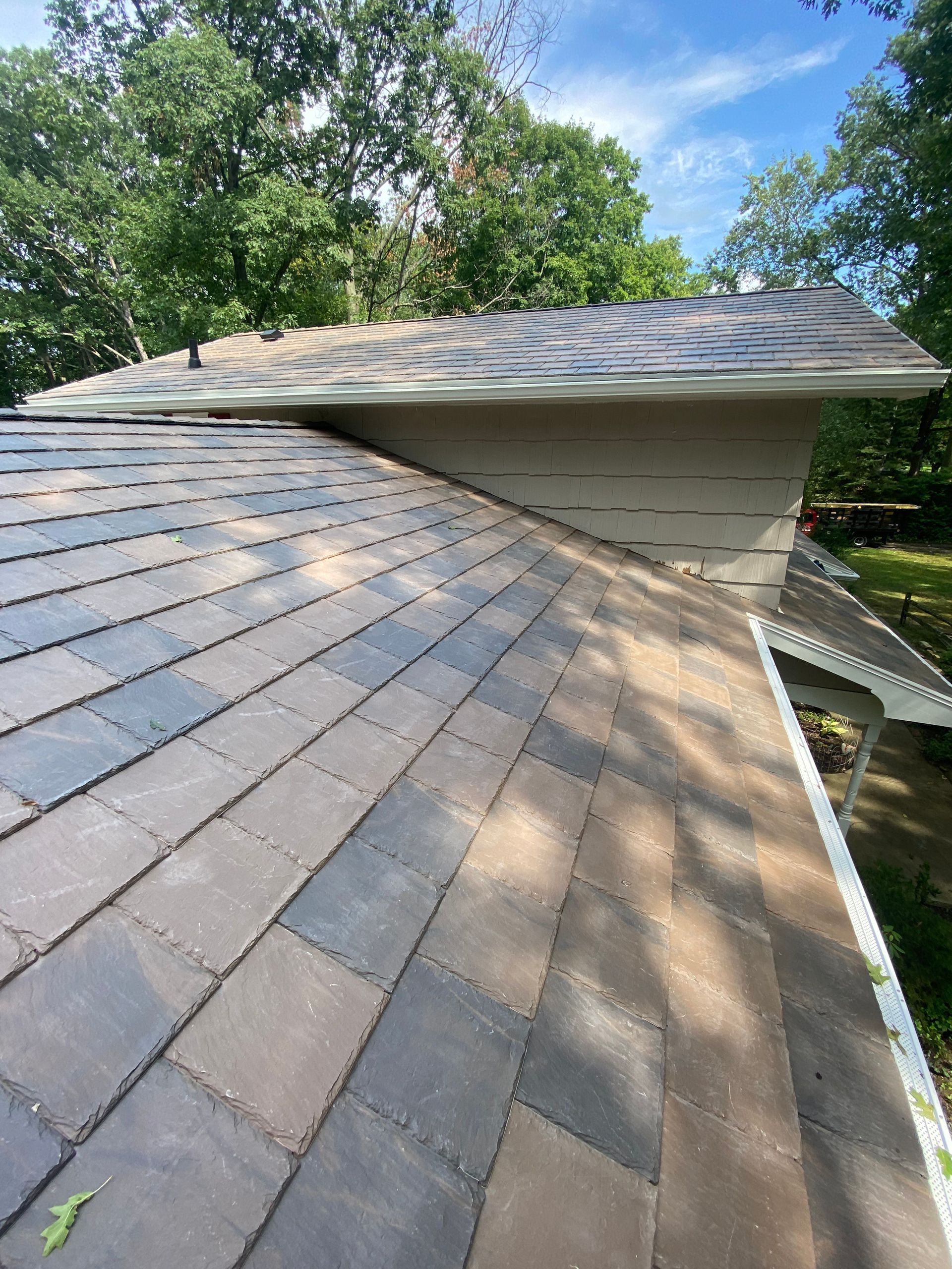 A close up of a roof with a gutter and trees in the background.