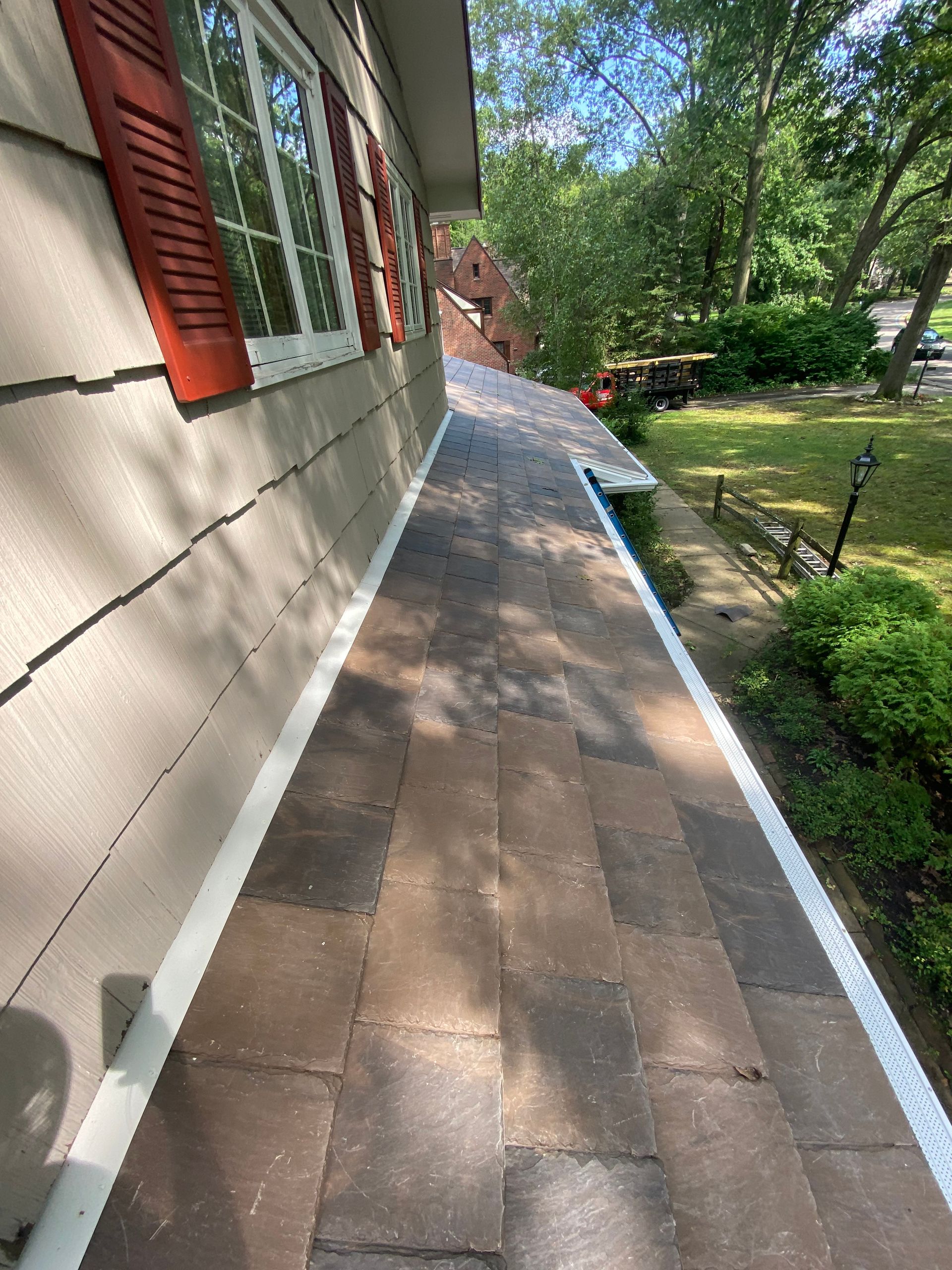 A sidewalk leading to the roof of a house with red shutters.