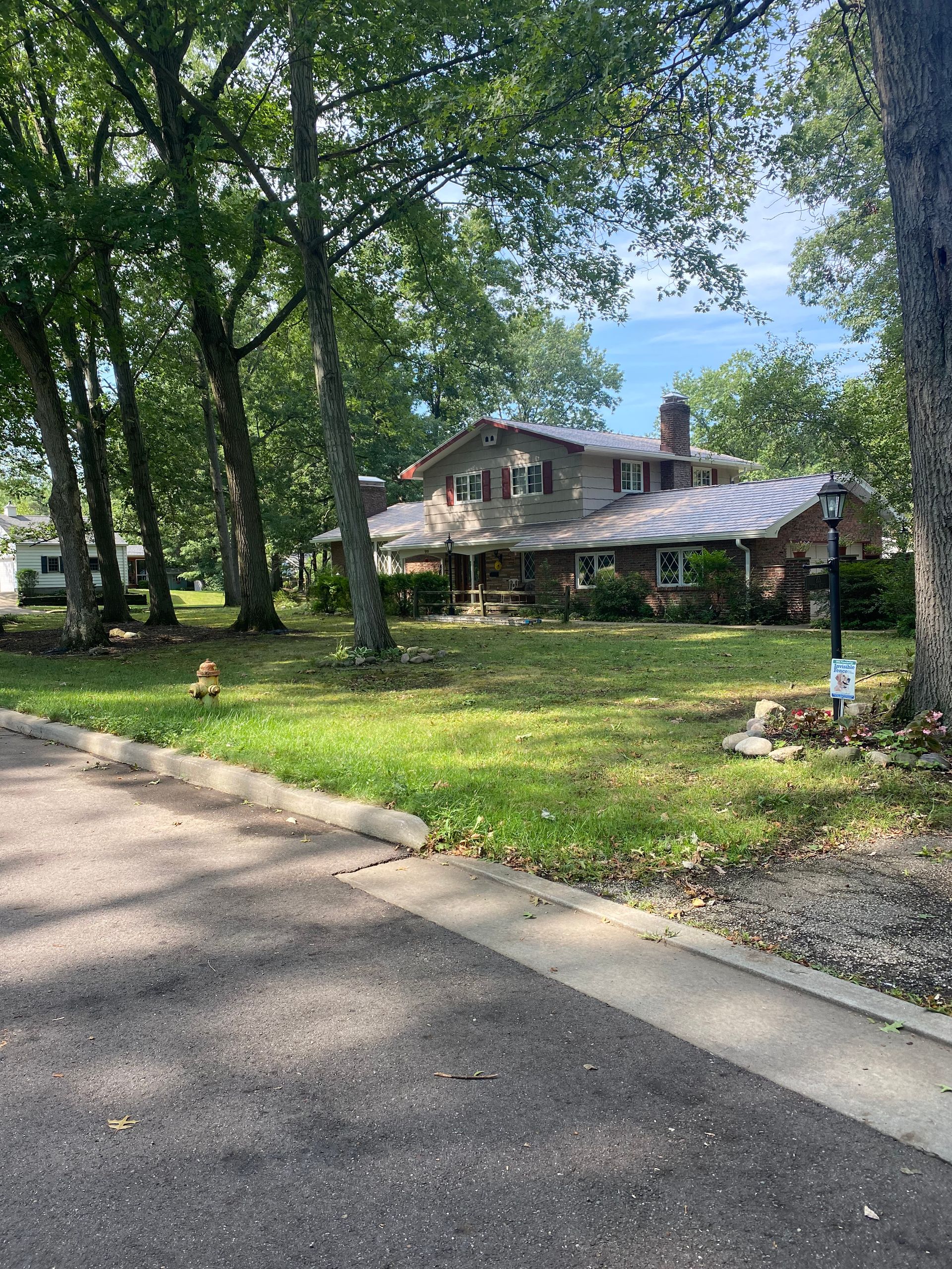 A large house is sitting on top of a lush green lawn surrounded by trees.