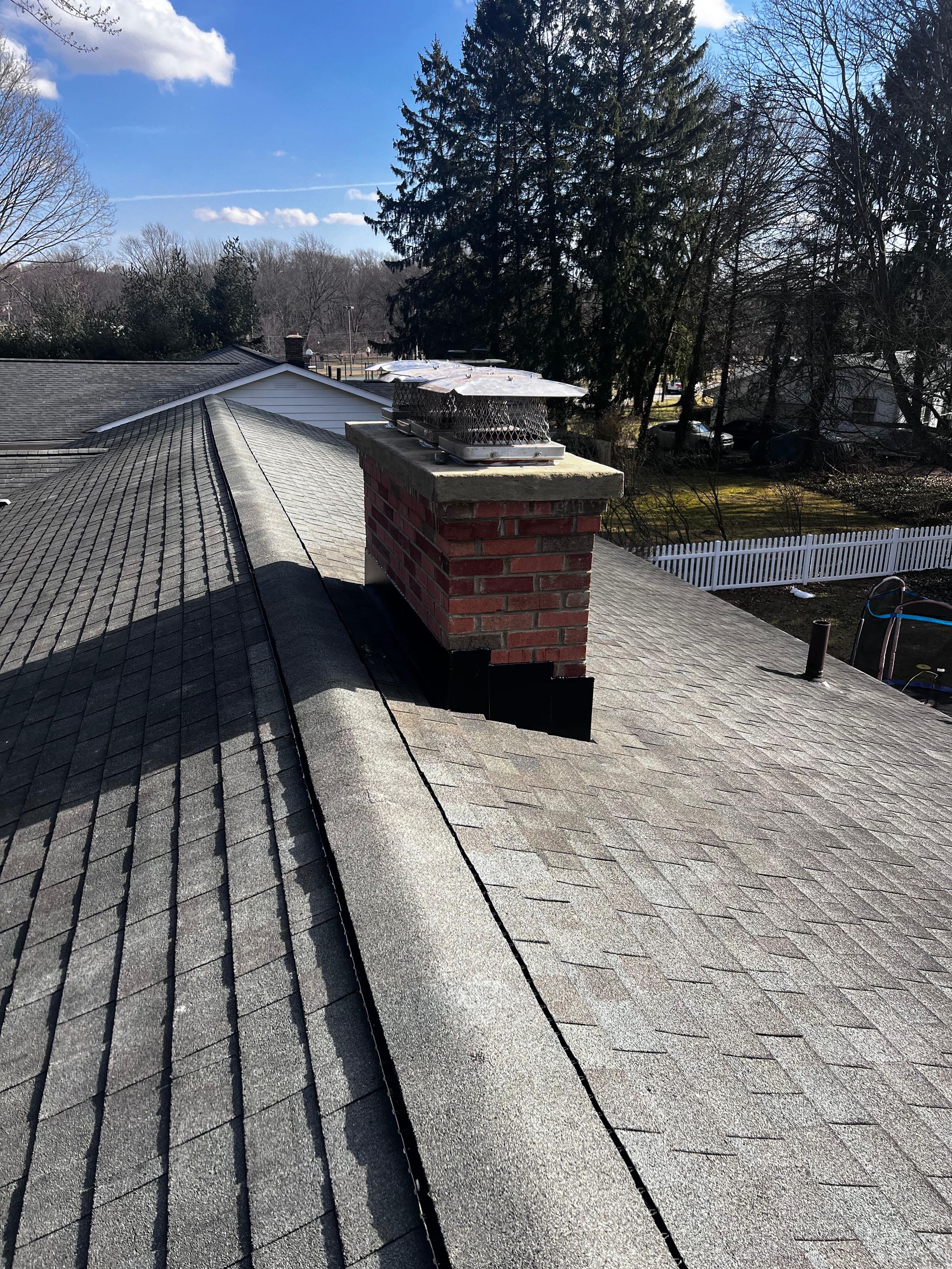 A brick chimney on top of a roof with trees in the background.