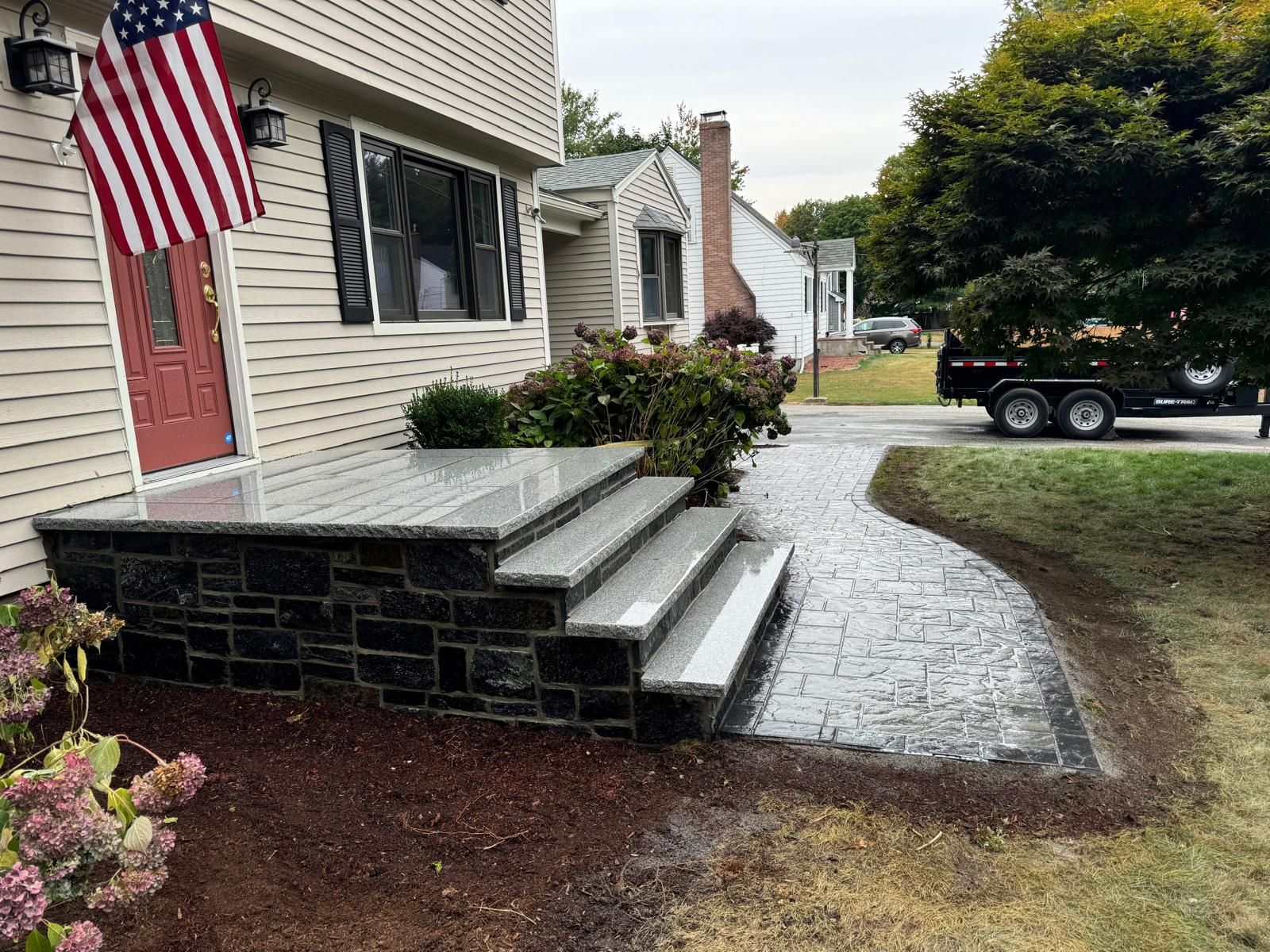 Front steps with granite treads and dark stone veneer, leading to a textured stone walkway outside a house.