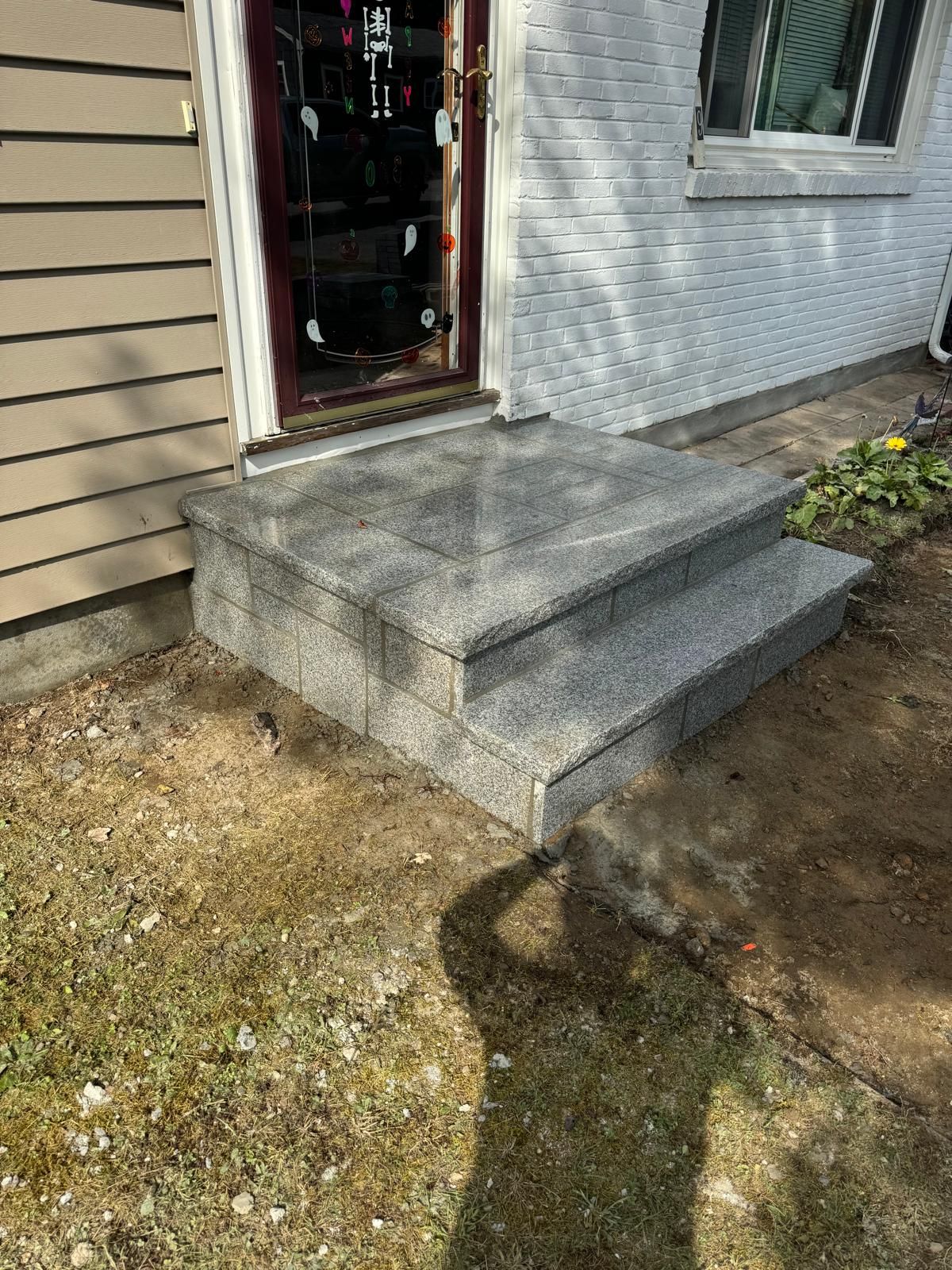 New granite front steps leading to a building entrance, set against beige siding and a white brick wall.