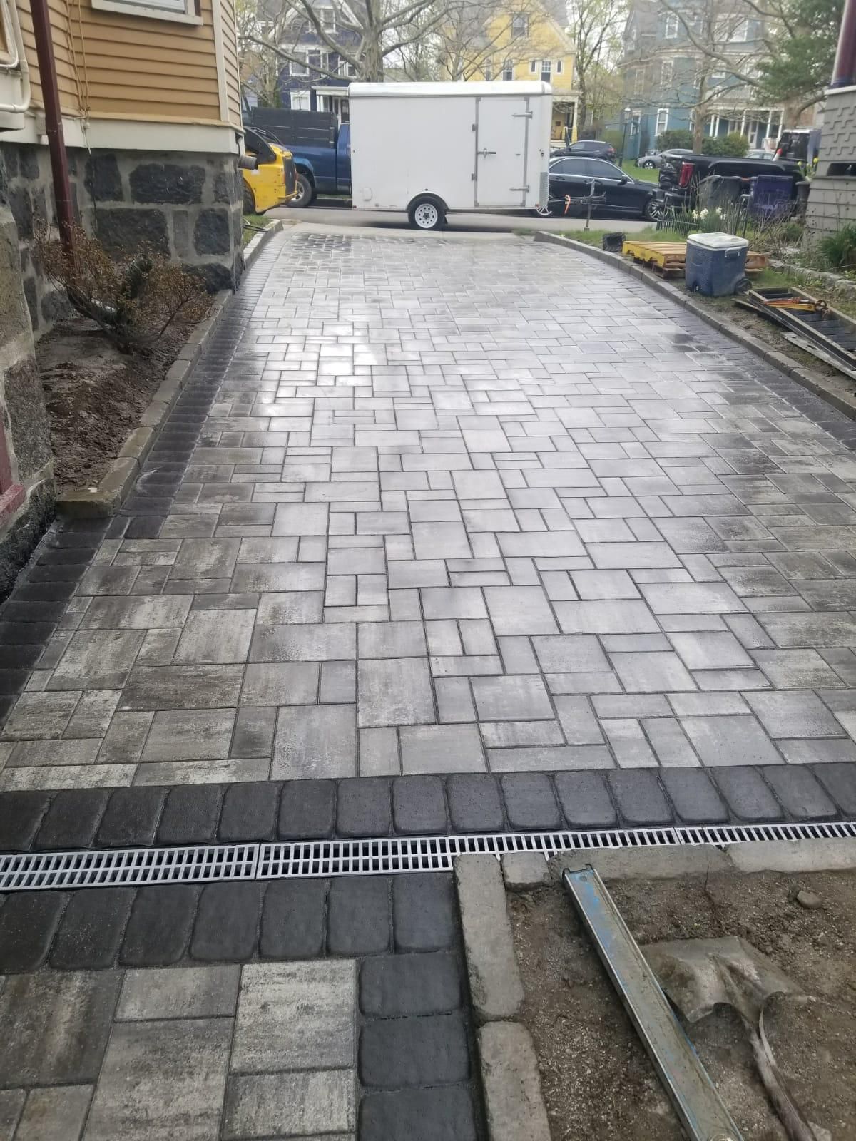 A newly paved stone driveway with a gray-toned patterned surface, dark stone border, and an integrated drainage grate.