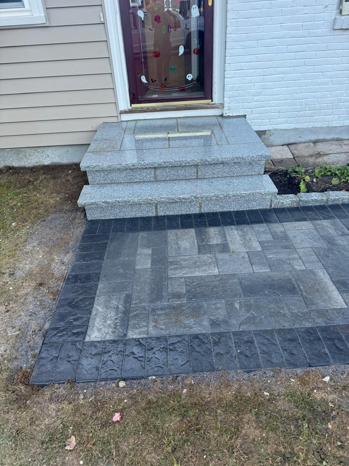 New gray granite front steps leading to a house door, bordered by a dark gray stone patio area.