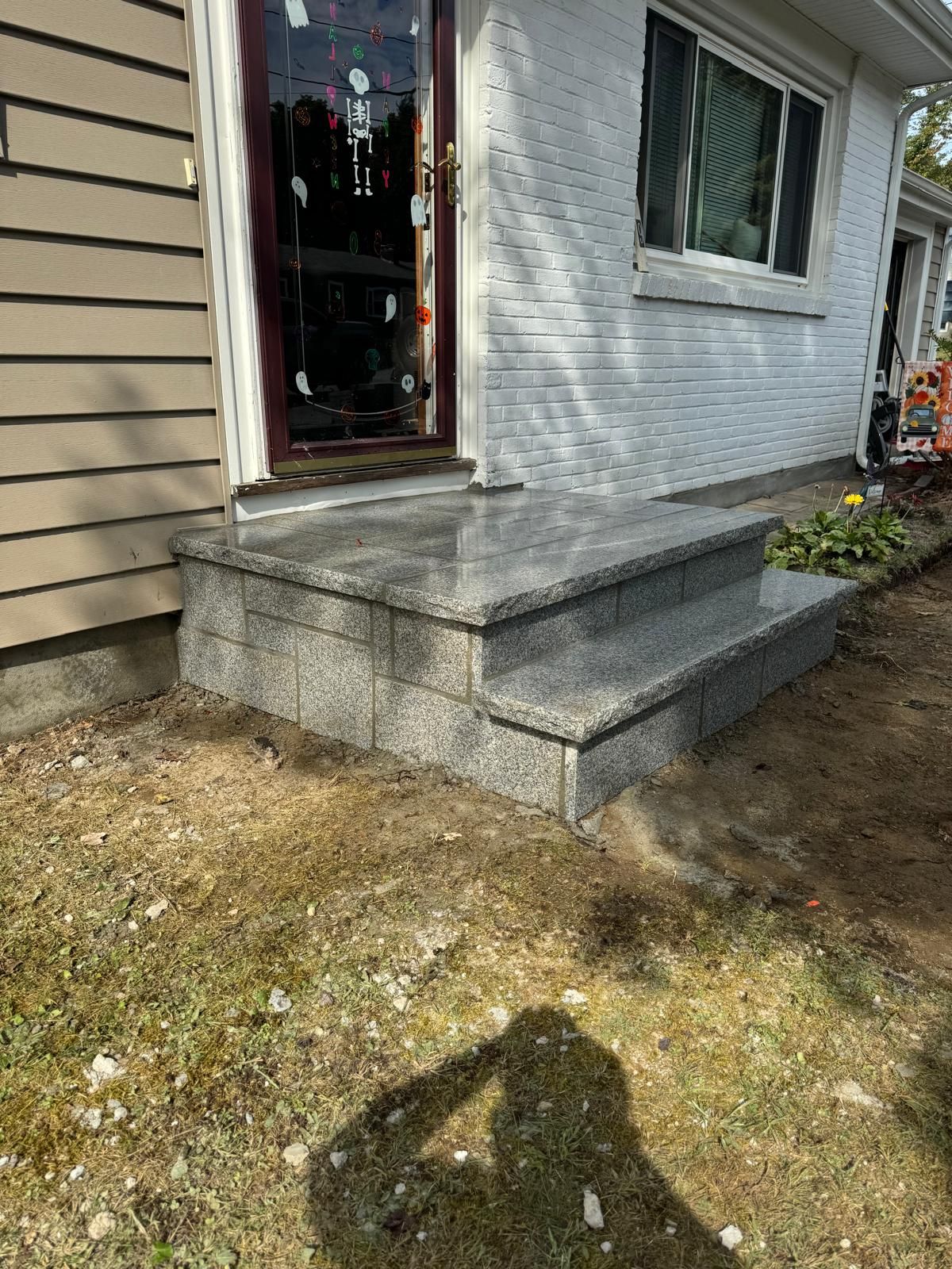 New granite steps installed at the front entrance of a house with white brick siding and tan vinyl siding.
