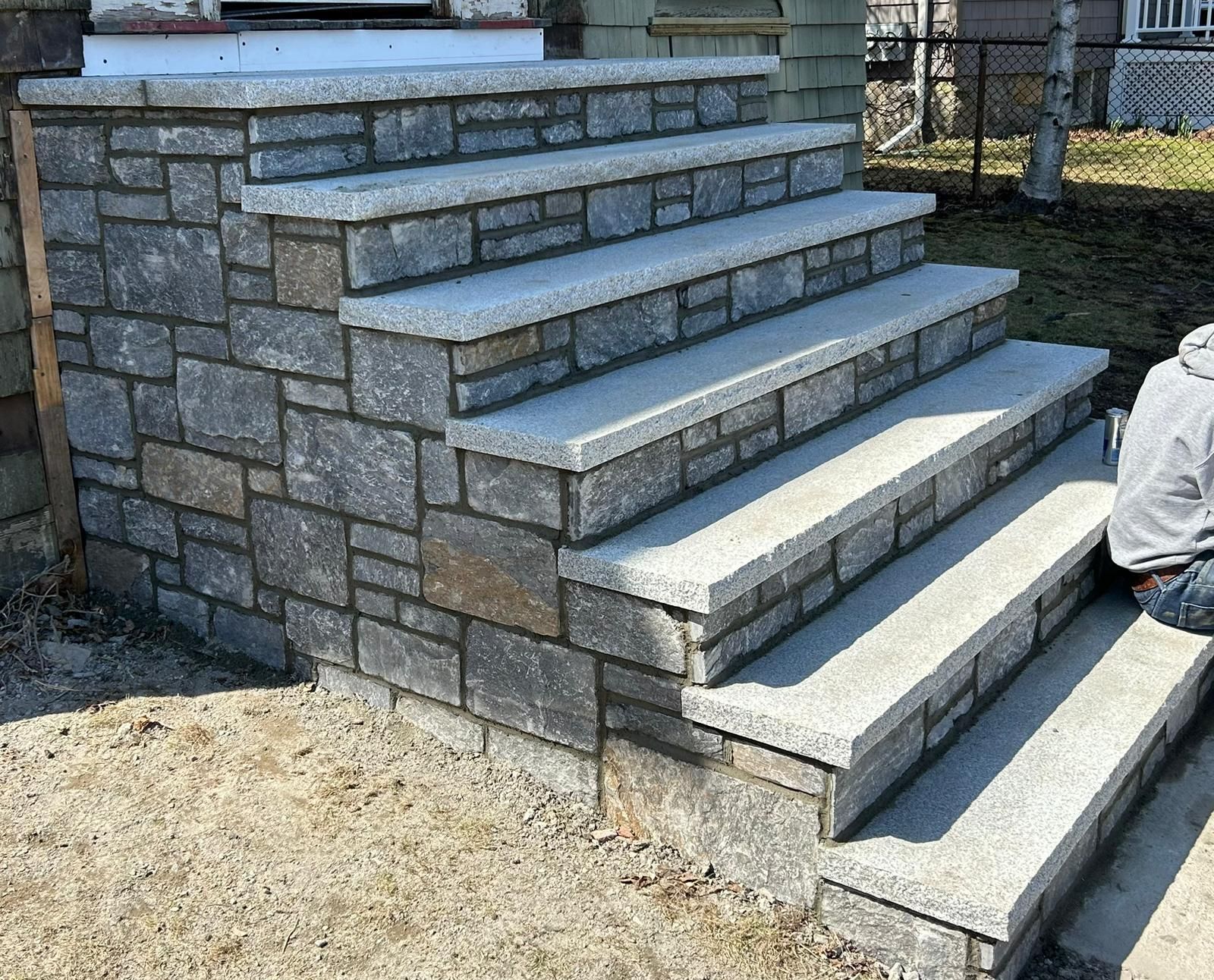 A new set of stone stairs with light grey granite treads and multi-toned, rectangular stone veneer risers and sides.