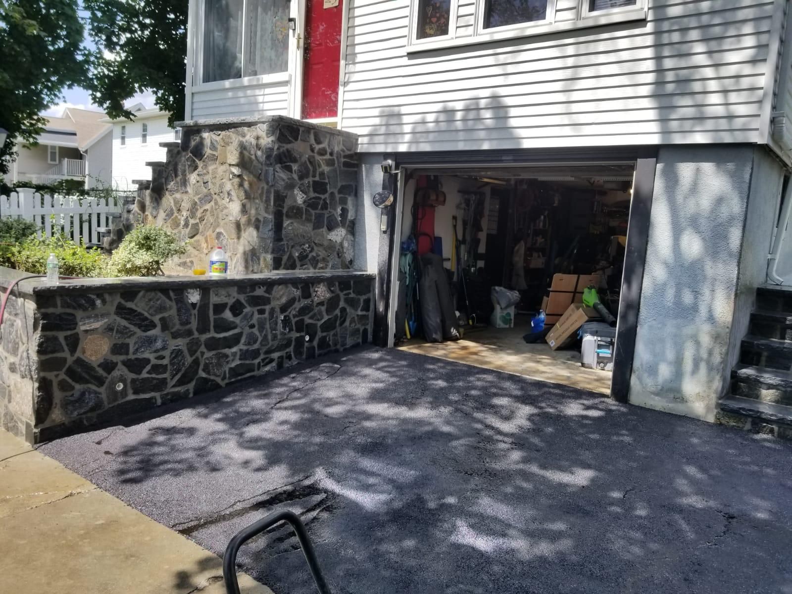 A house exterior showing a stone retaining wall, a freshly laid gravel driveway, and an open garage bay.