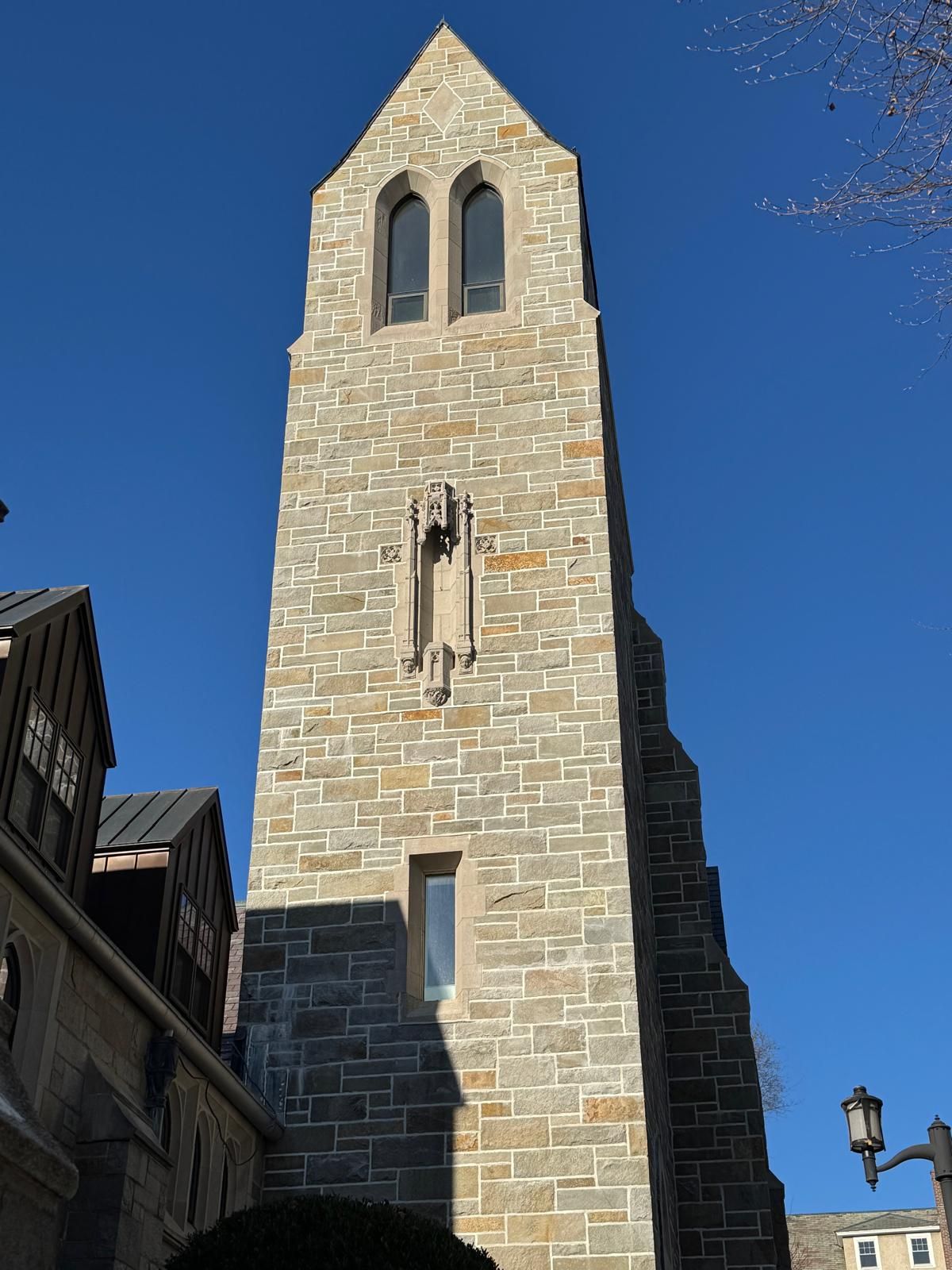 A tall, stone tower featuring a pointed top, narrow windows, and intricate masonry under a clear blue sky.