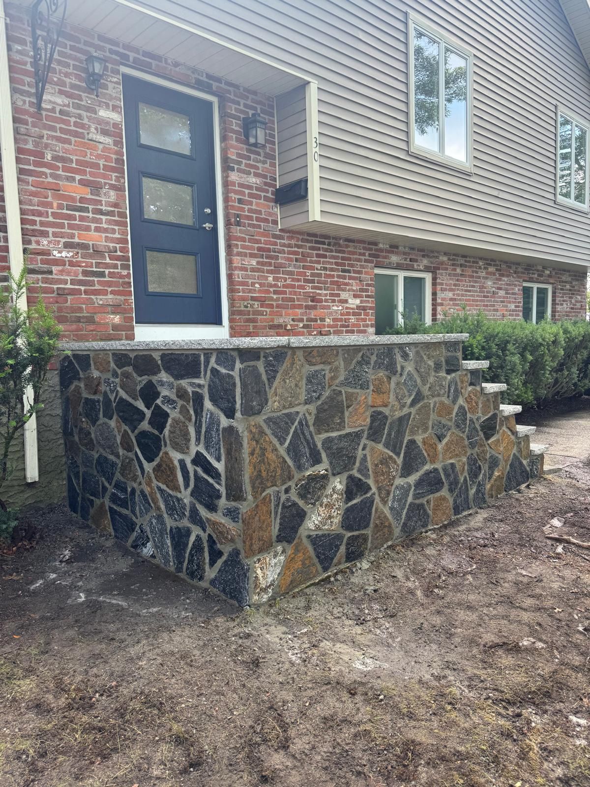 A home exterior featuring a front entrance with new stone veneer steps leading to a dark blue door with three glass panes.
