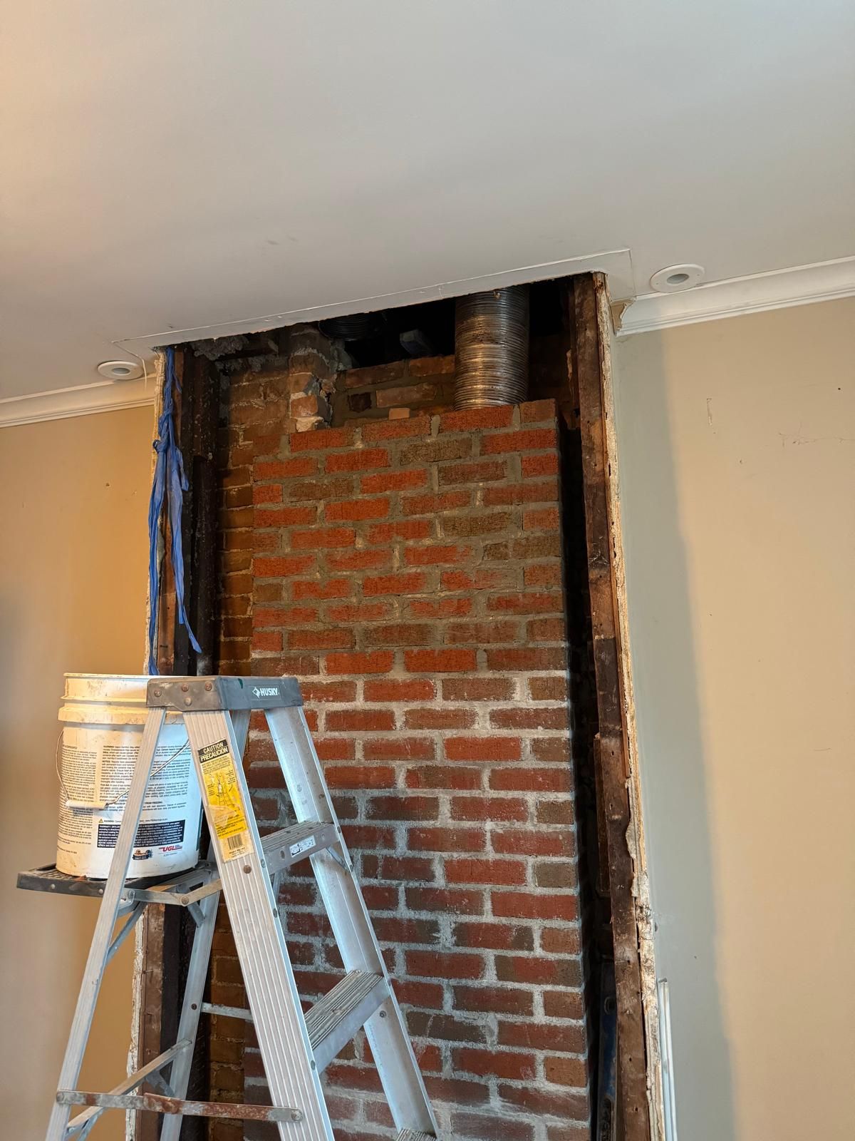 A white stepladder stands before an exposed interior brick chimney breast in a room undergoing construction.