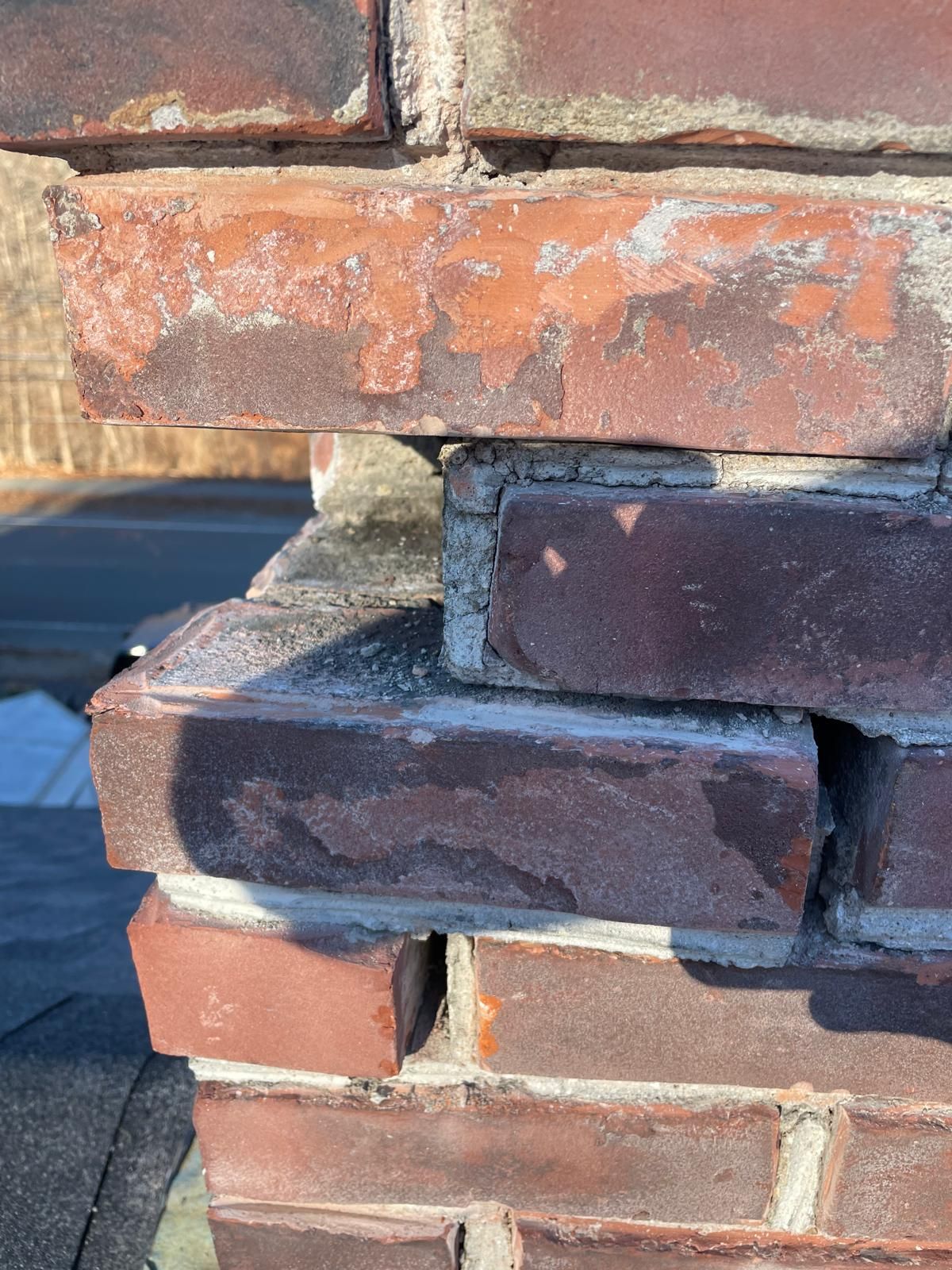 Close-up of a damaged brick chimney with crumbling mortar and misaligned, weathered bricks.