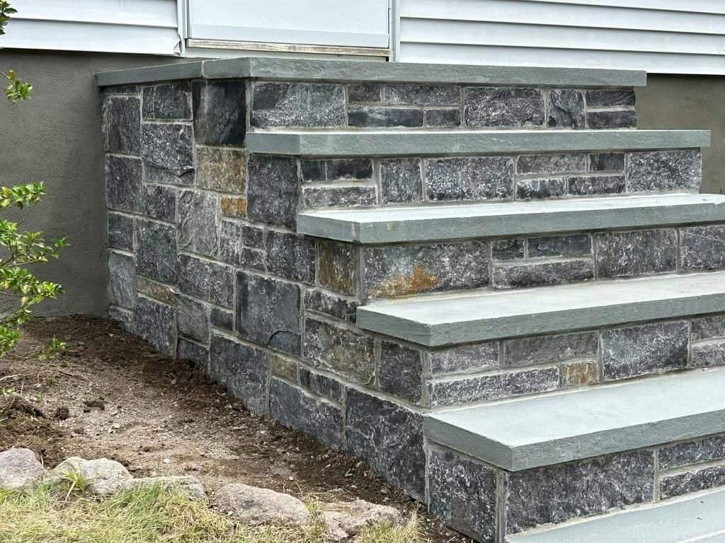 Exterior stone steps with grey, rectangular treads leading to a white house door.